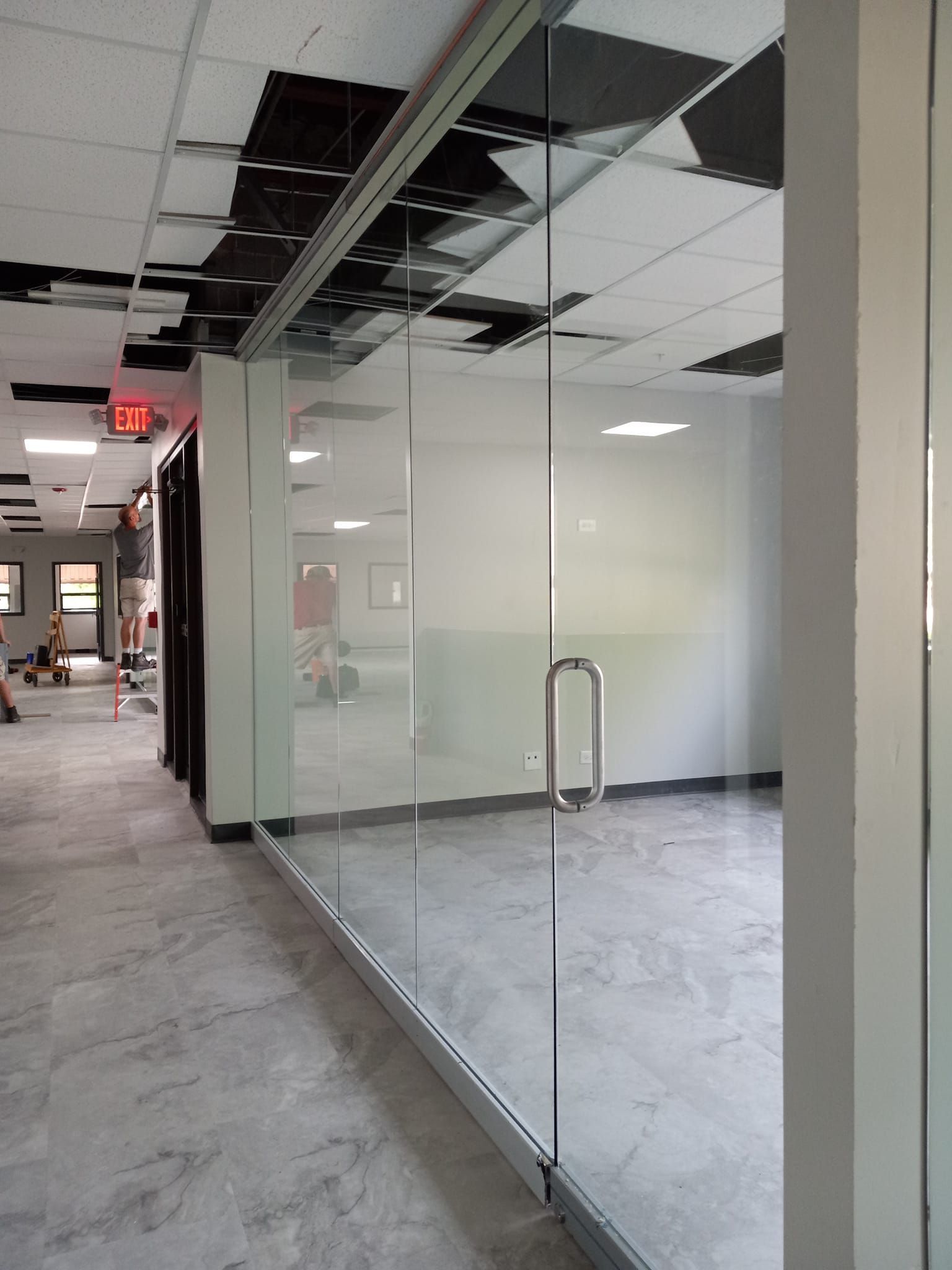 Glass-walled office space under construction, with open ceiling and gray tile floors.
