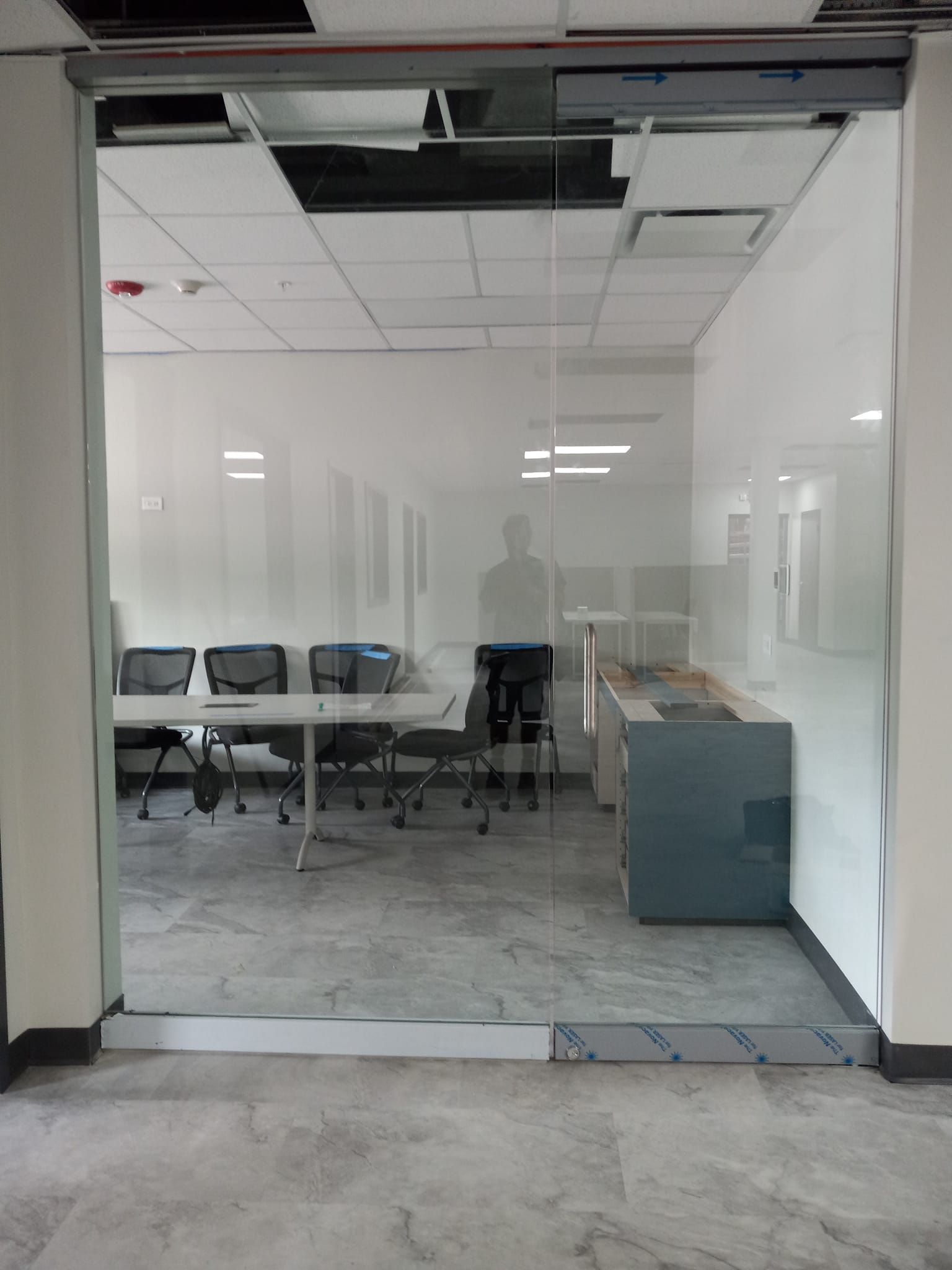 Glass-walled office: conference table, chairs, cabinets, visible through open doorway. Gray floors, white walls.