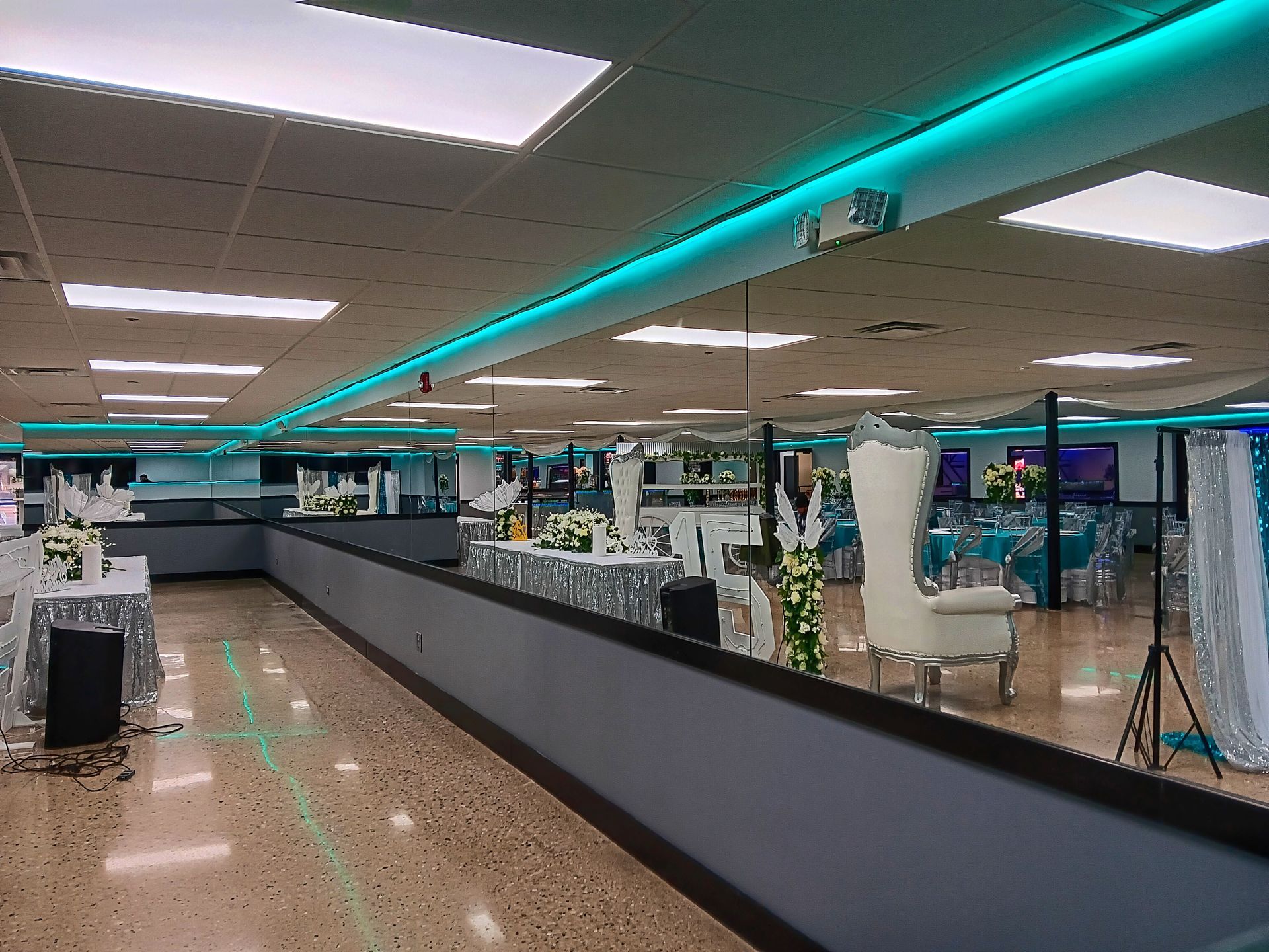 Large event space with teal and white decor, tables set, long grey barrier.