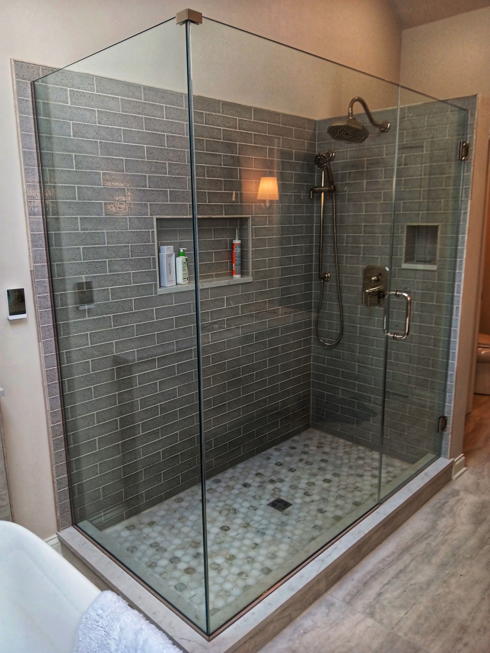 Glass-walled shower with gray tiled walls, stone floor, and built-in shelves.