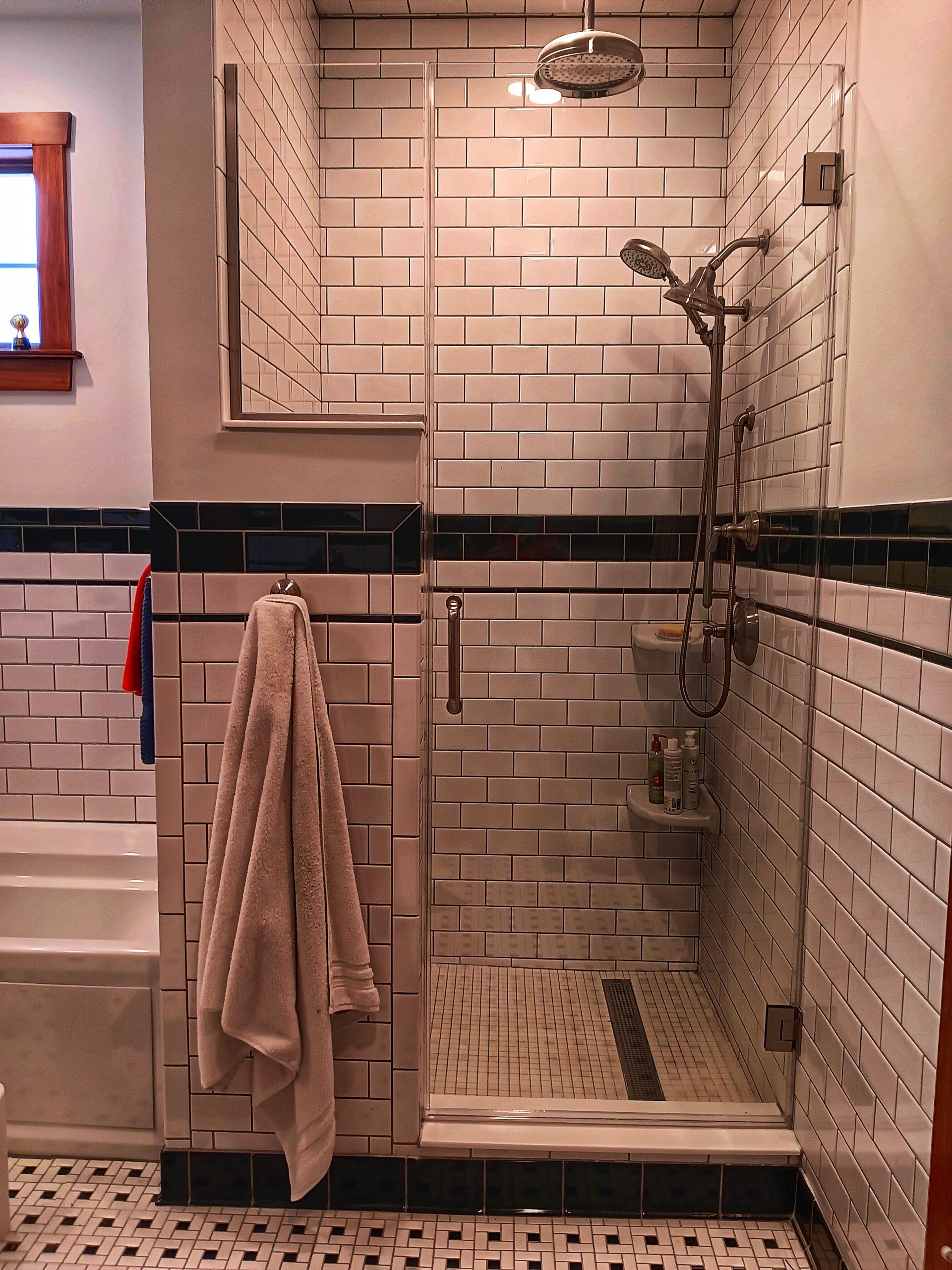 Shower with white brick tiles, glass door, and silver shower head. A towel hangs outside the shower.