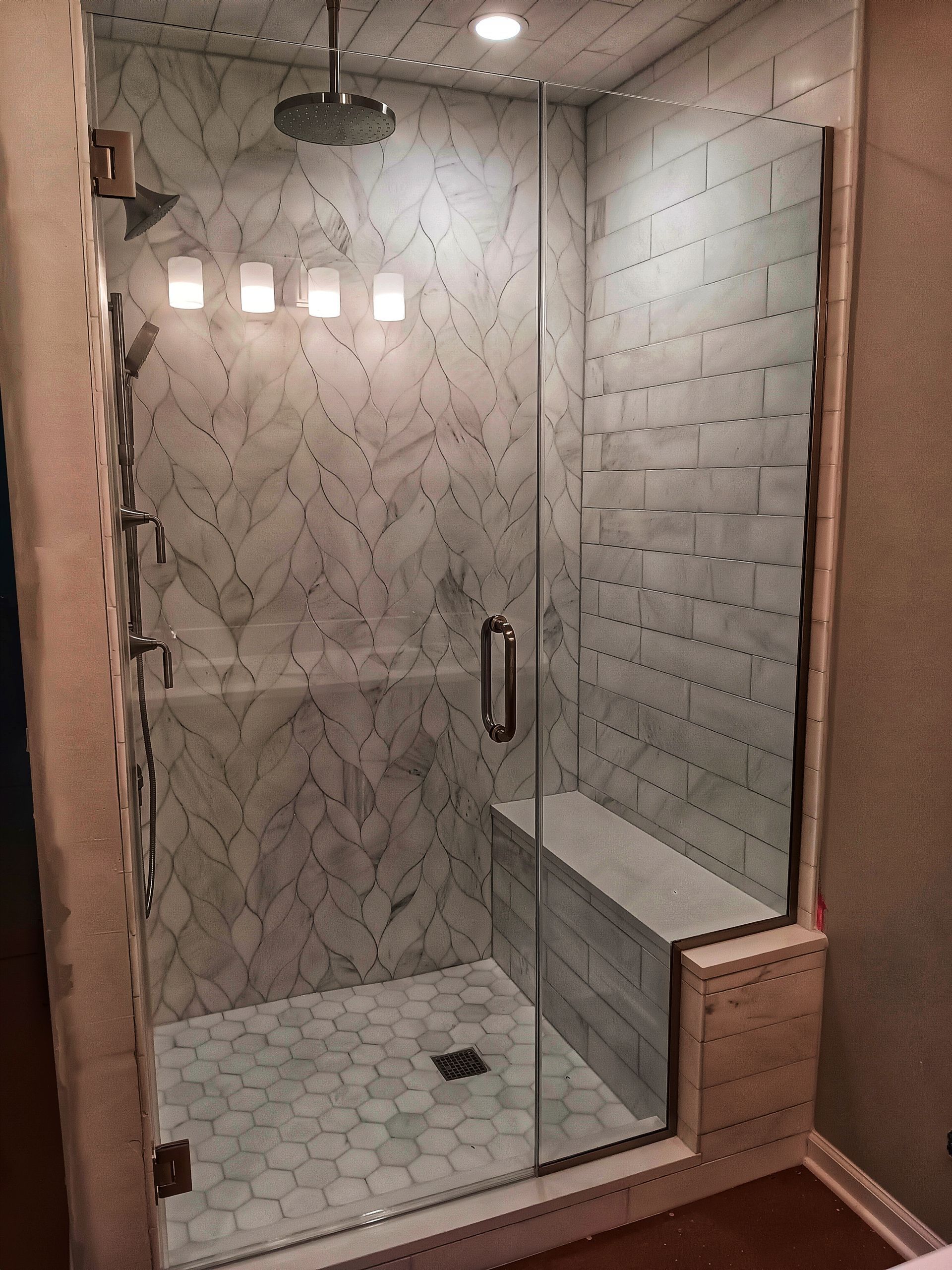 Modern glass shower with gray and white tile, a bench, and a rain showerhead.