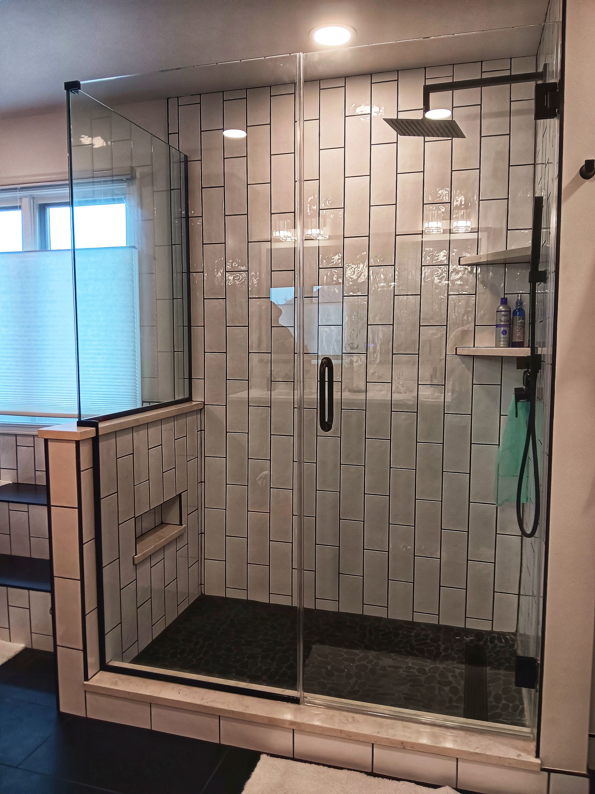 Glass shower with patterned white tile walls, black floor, and dark hardware.