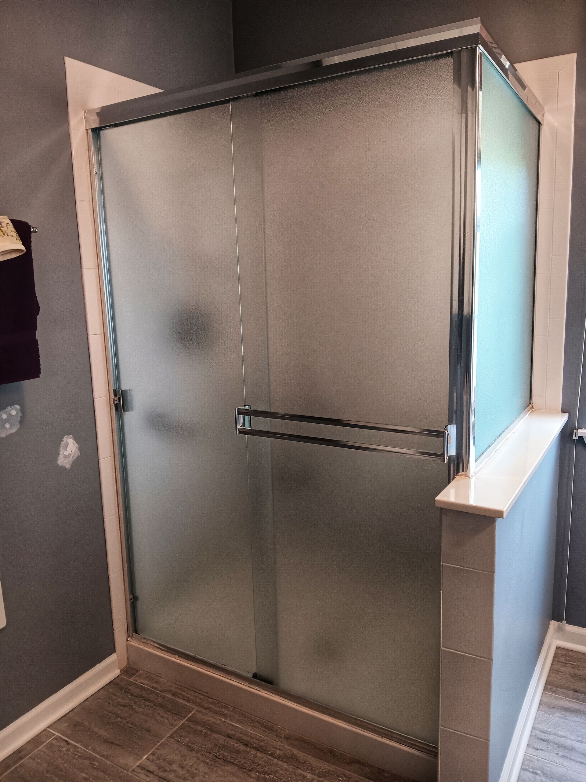 Frosted glass shower enclosure with chrome trim in a gray-tiled bathroom.