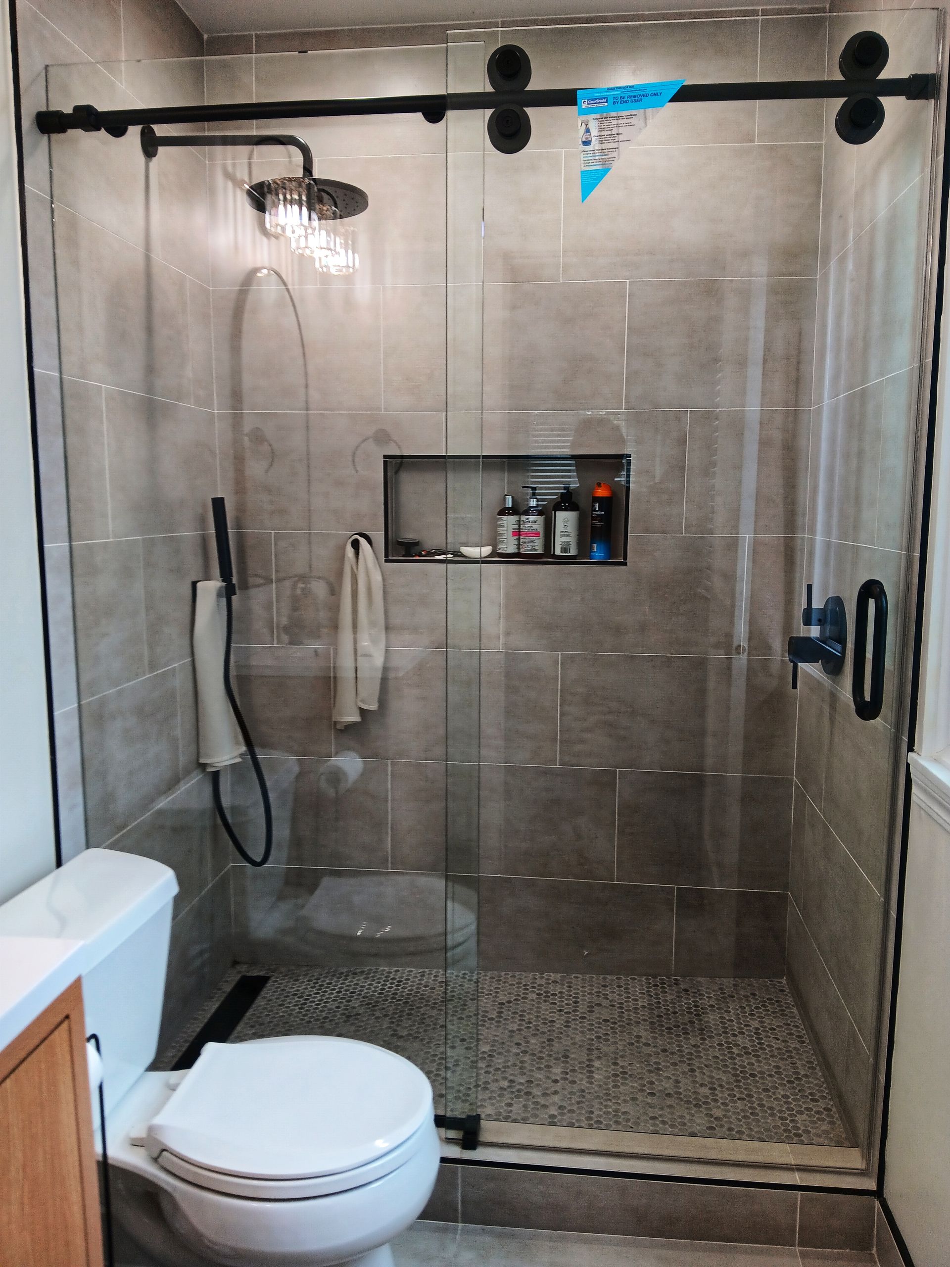 Bathroom with glass shower, pebble floor, built-in shelf, and black sliding door hardware.