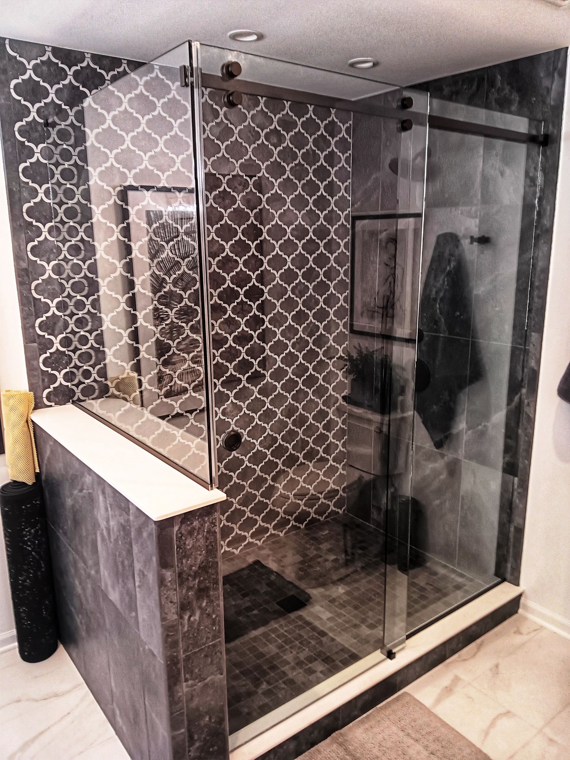 Modern bathroom with a glass shower, dark tile walls with a decorative pattern, and a black towel.