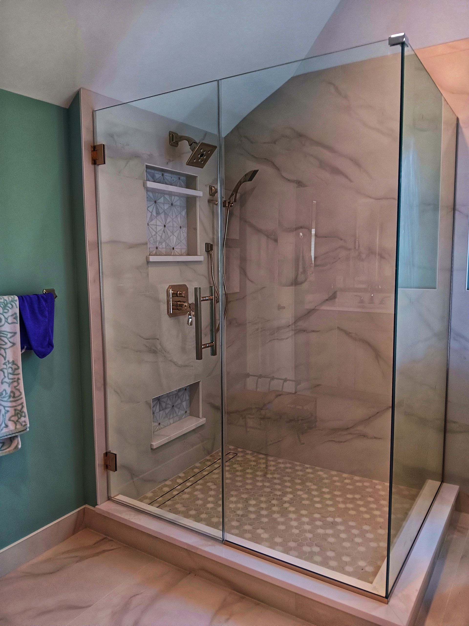 Glass shower enclosure with marble tile, gold fixtures, and pebbled floor.