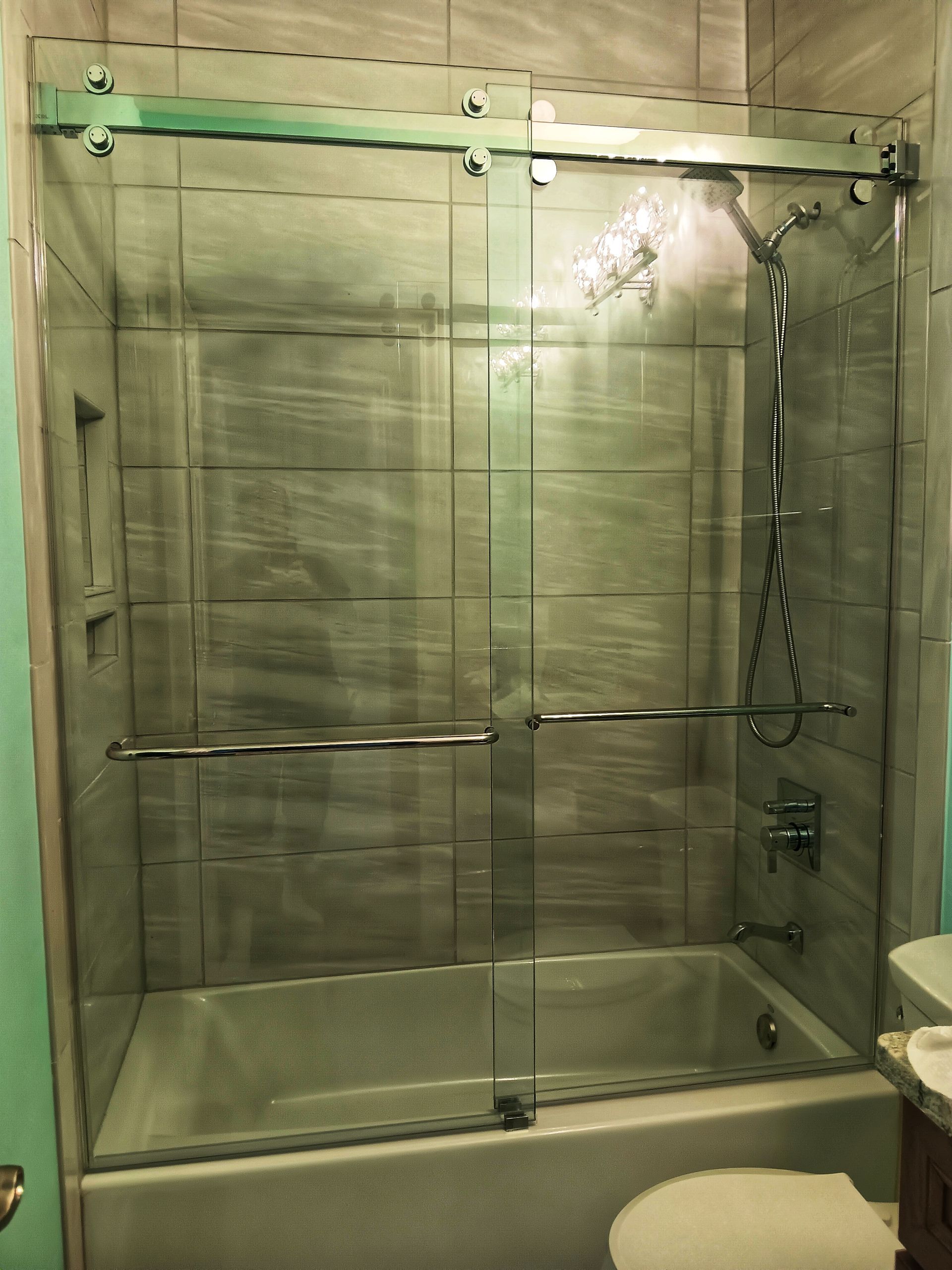 A shower with sliding glass doors, a white bathtub, and gray tiled walls.