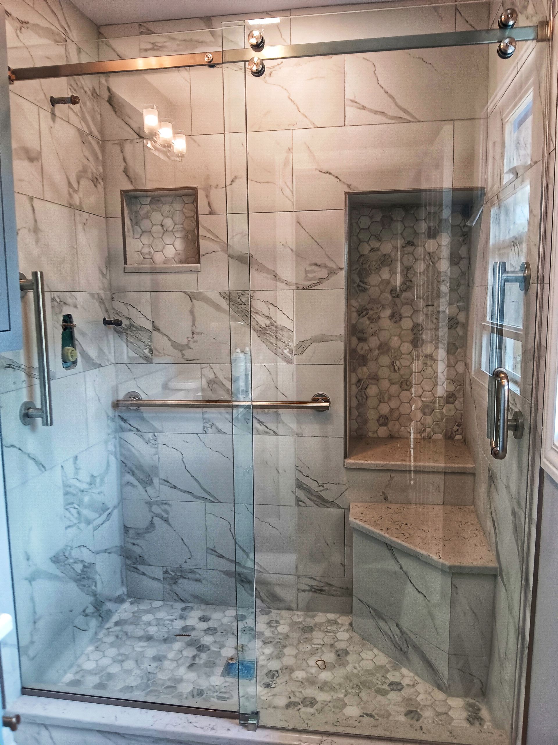 Marble-tiled shower with a glass door, built-in bench, and niche. Includes bronze hardware and recessed lighting.