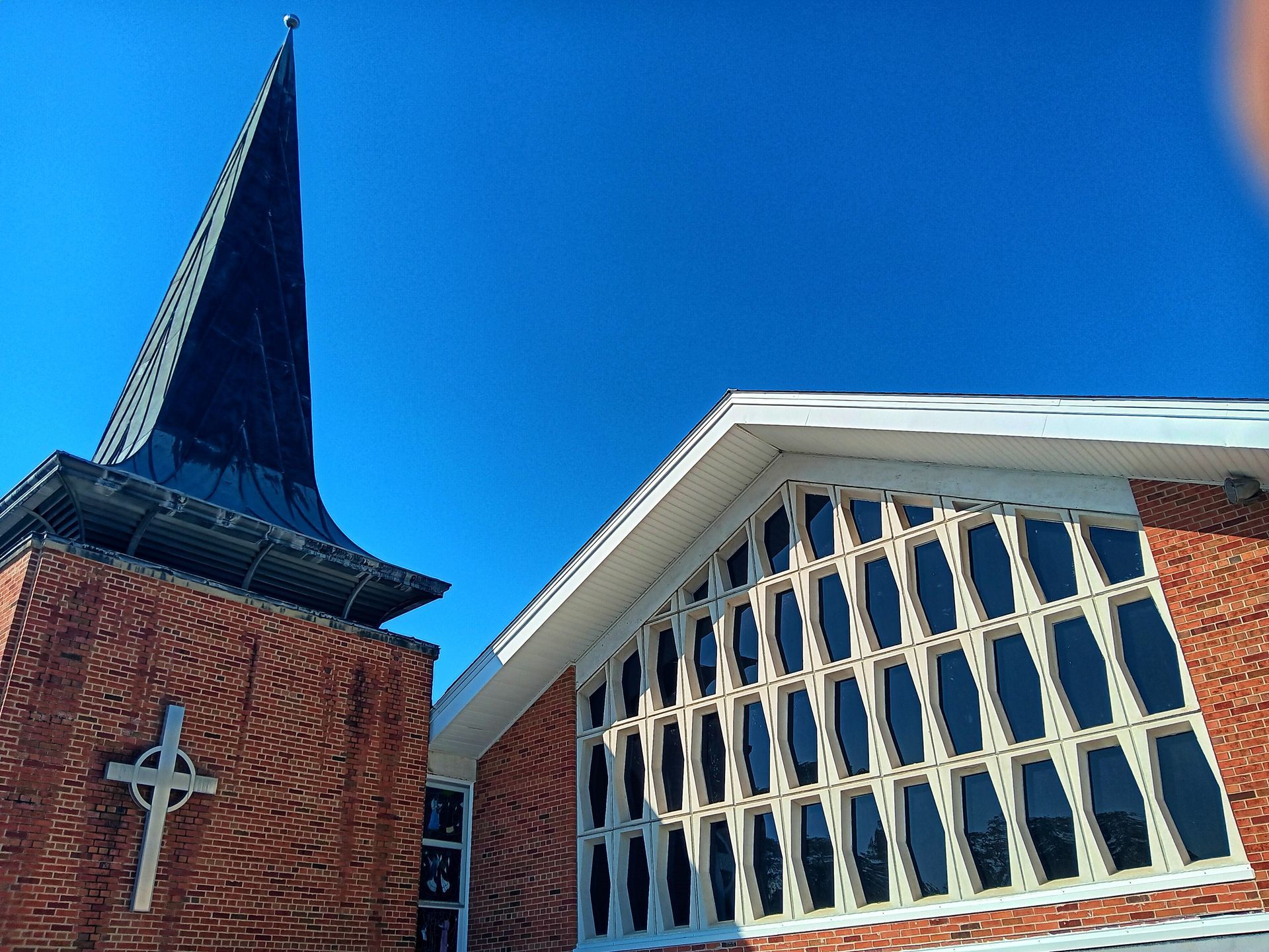 Church building with a tall spire and large windows against a blue sky.