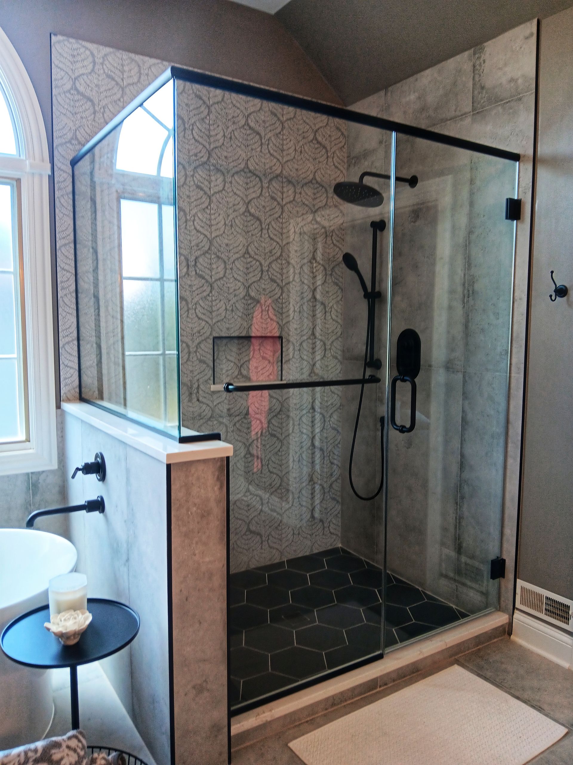 Modern bathroom with glass shower enclosure, black fixtures, and patterned tile.