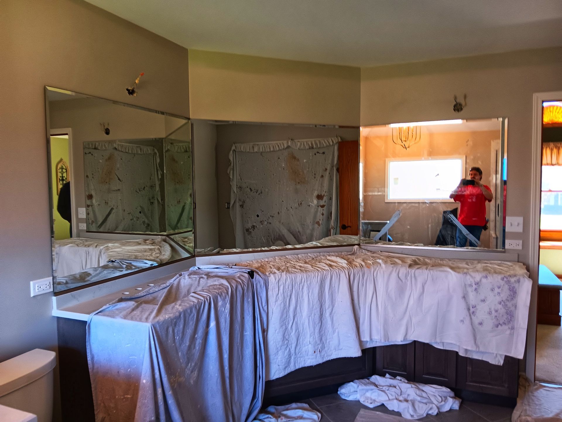 Bathroom with large mirrors, cabinets, and a person in a red shirt working on something.