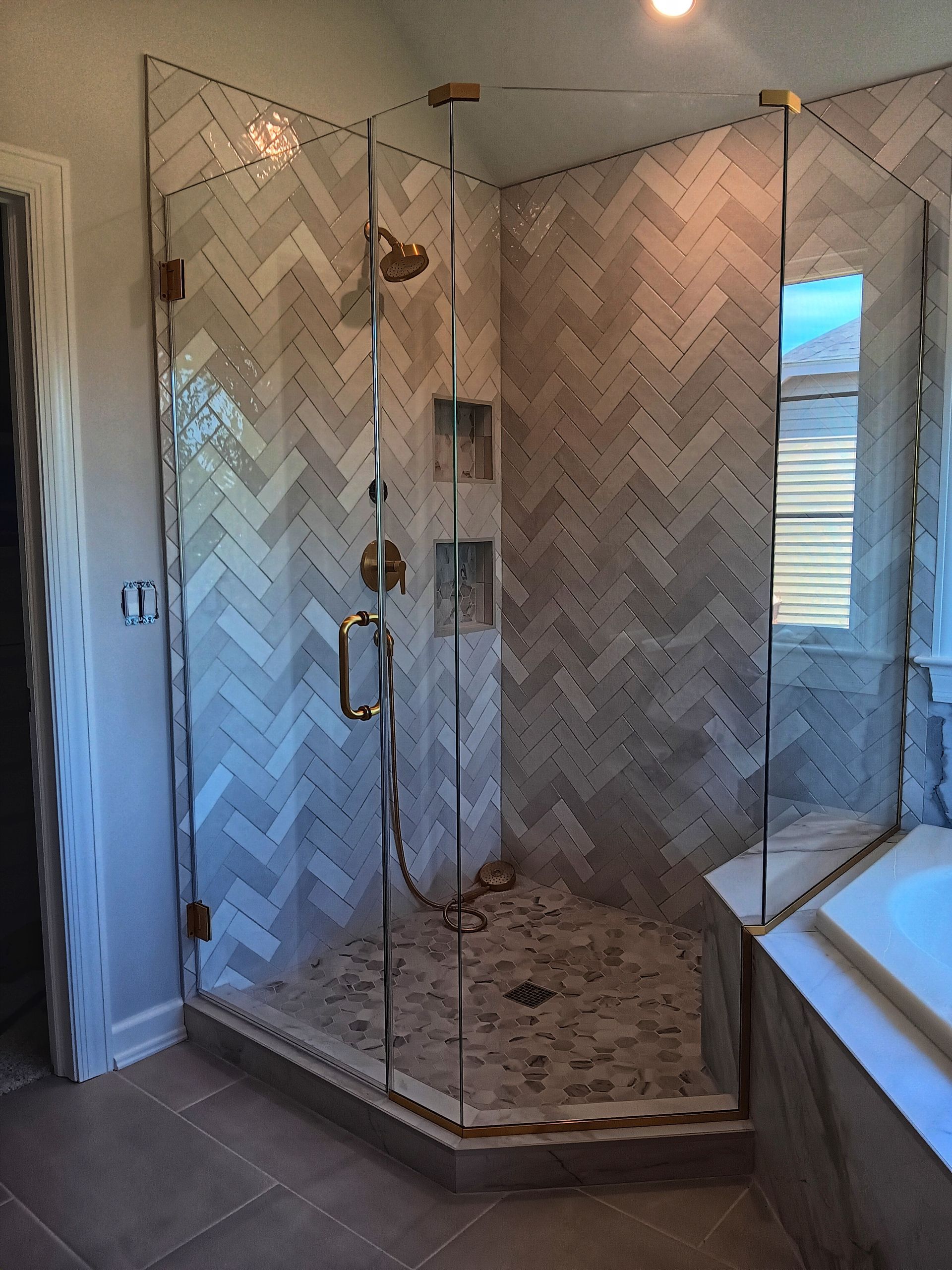 A modern shower with clear glass doors and herringbone-patterned gray tile walls.