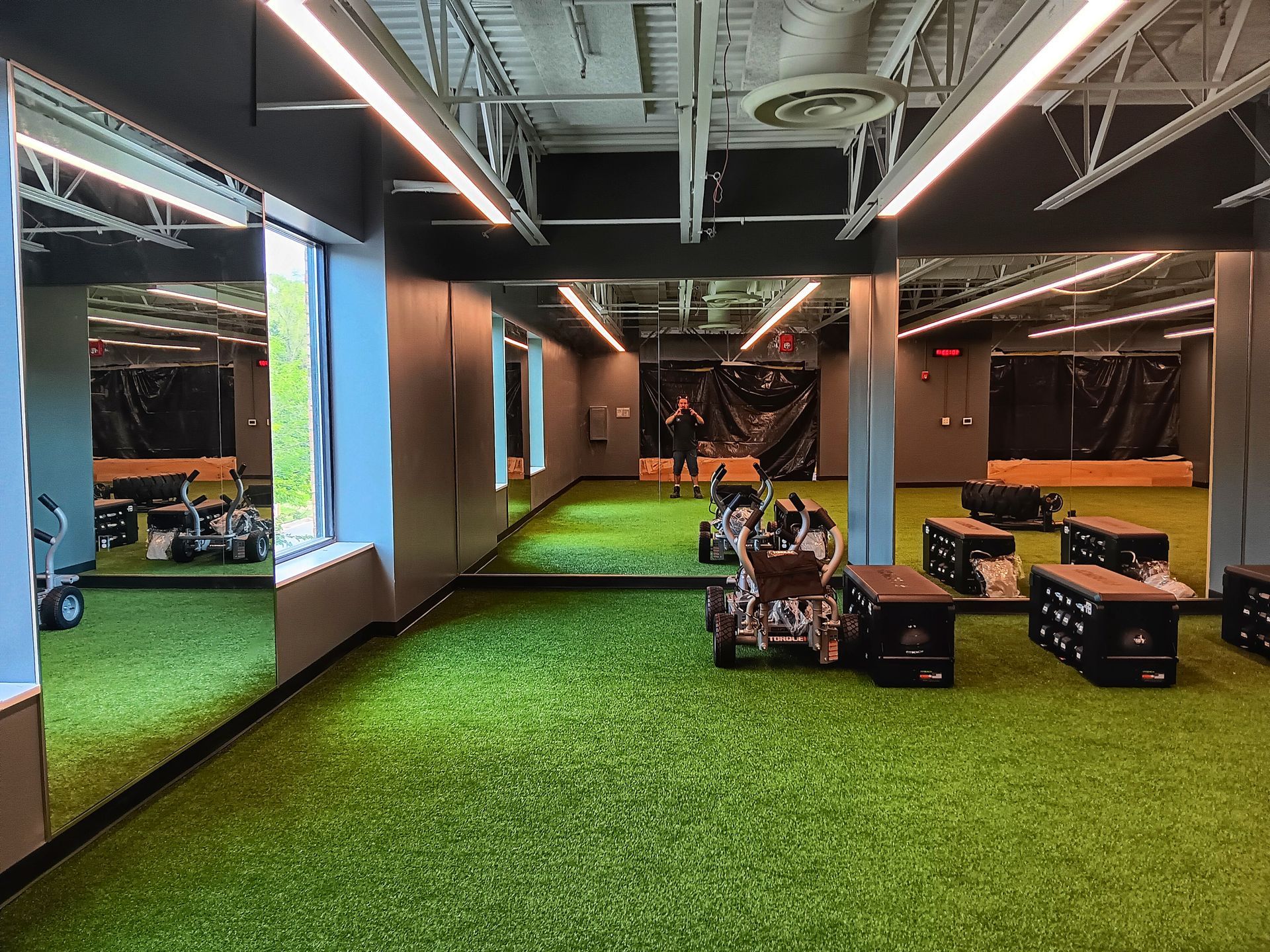 Indoor training facility with artificial turf, exercise equipment, and people.