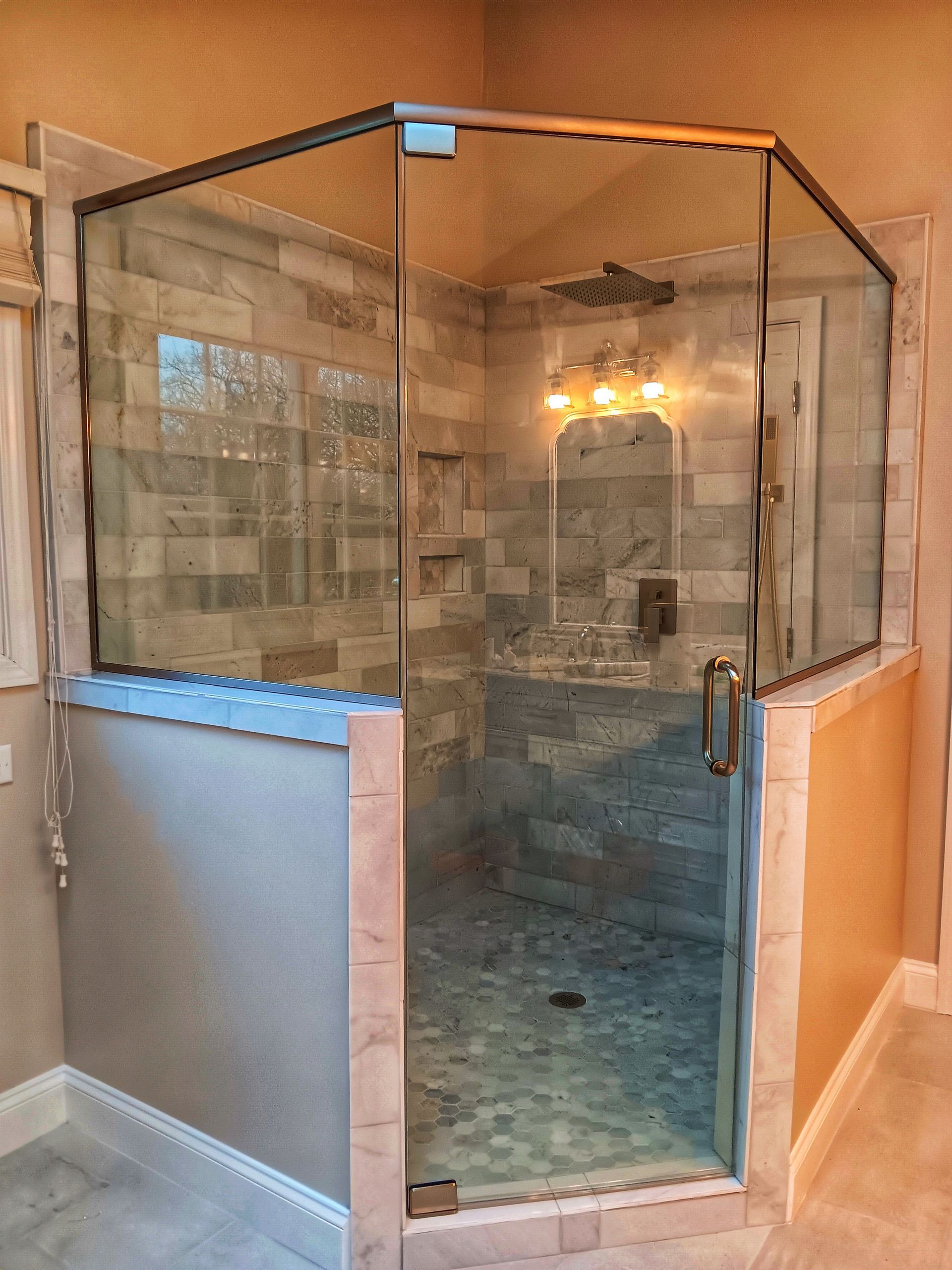 Glass-enclosed shower with tiled walls and a door; light fixtures and a window are visible.
