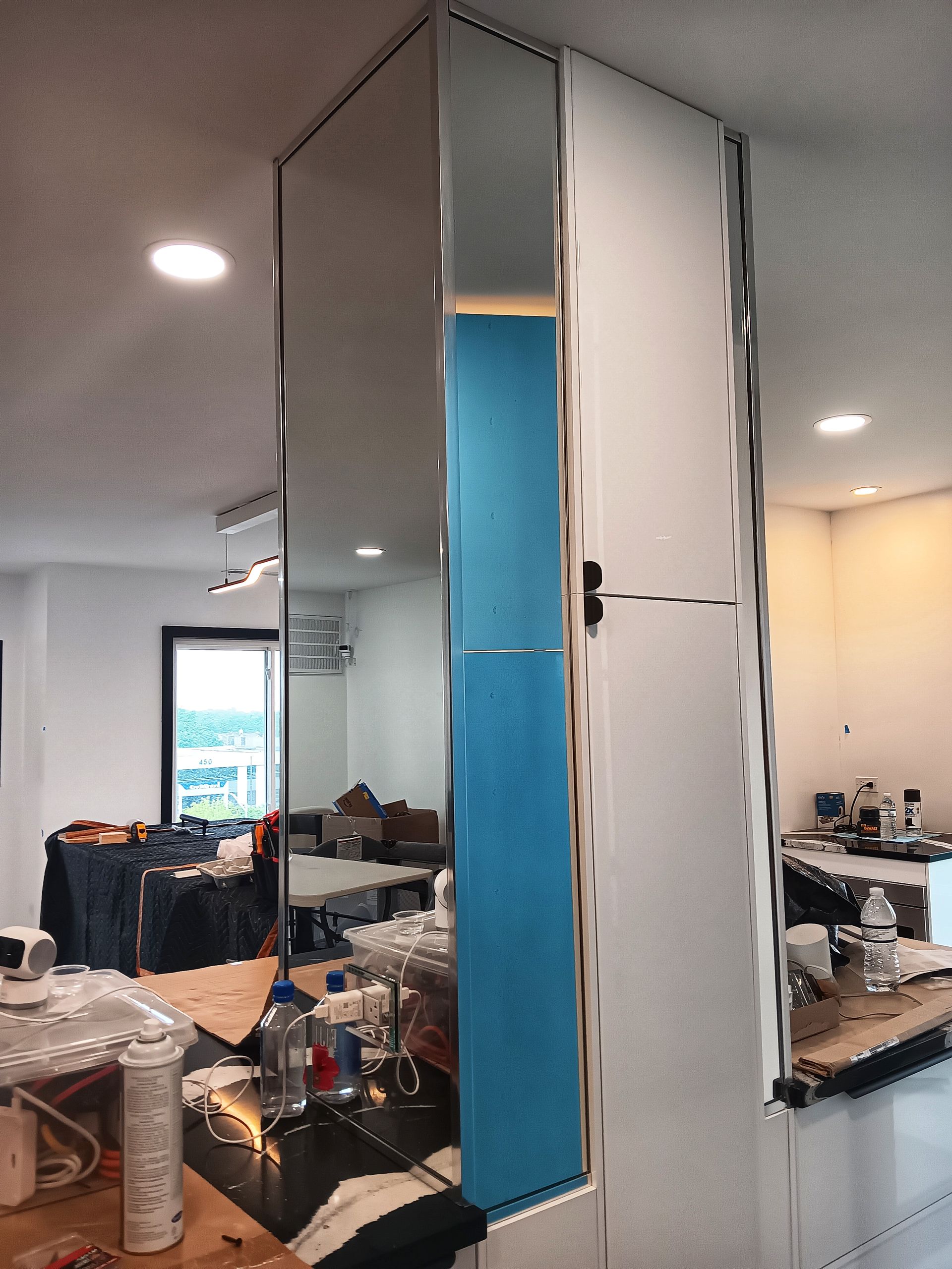 Mirrored corner with white cabinet and blue protection, in a kitchen area with work in progress.
