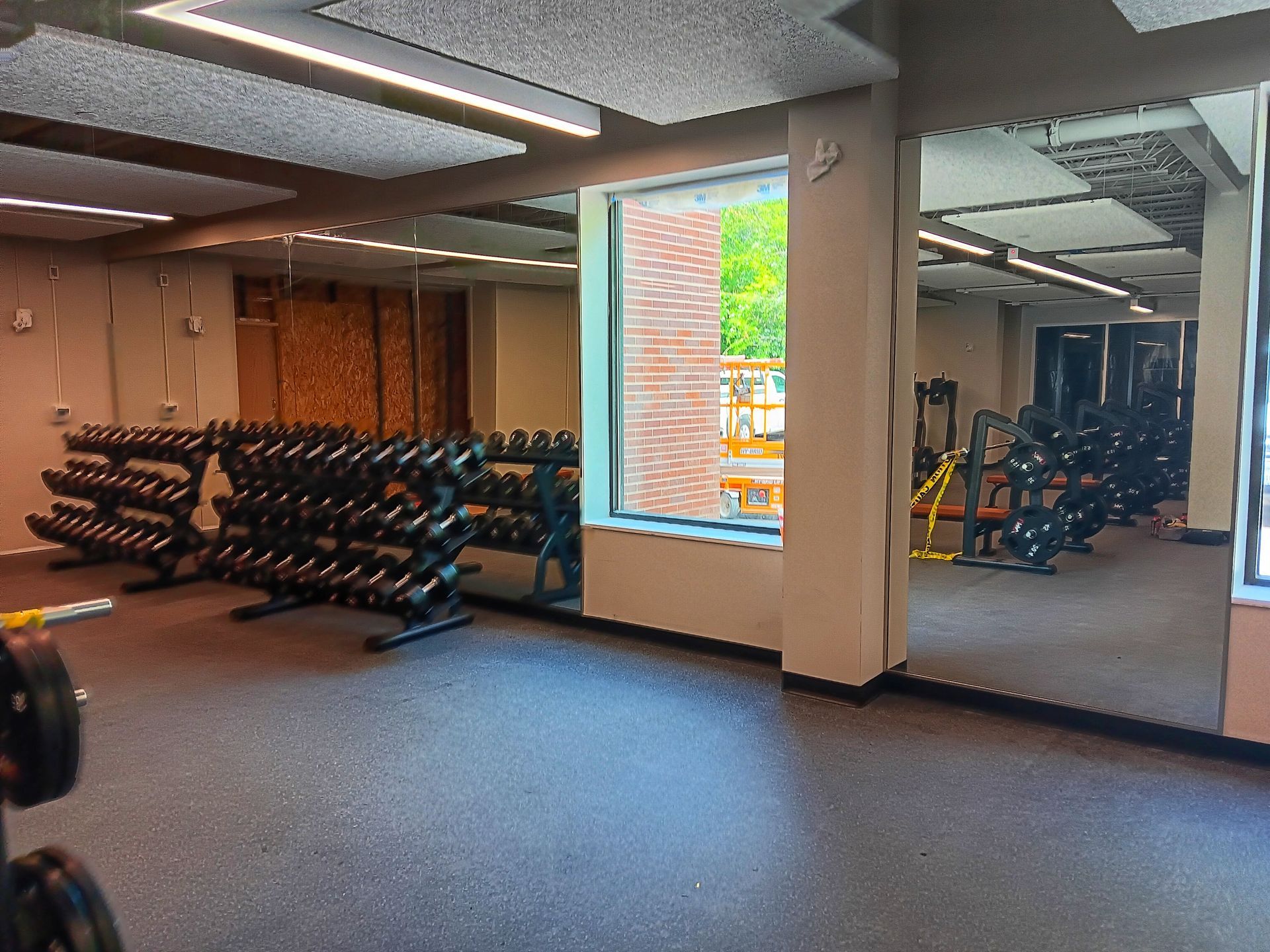 Gym with dumbbell racks, mirrors, and a window showing an outdoor patio.