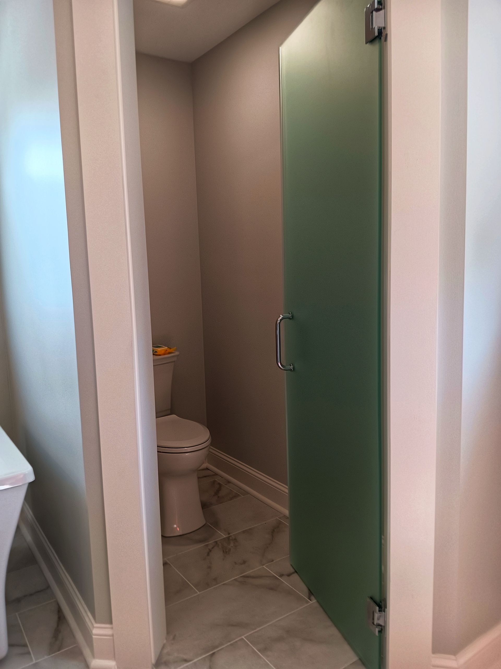 Powder room with frosted glass door, toilet, and gray walls.