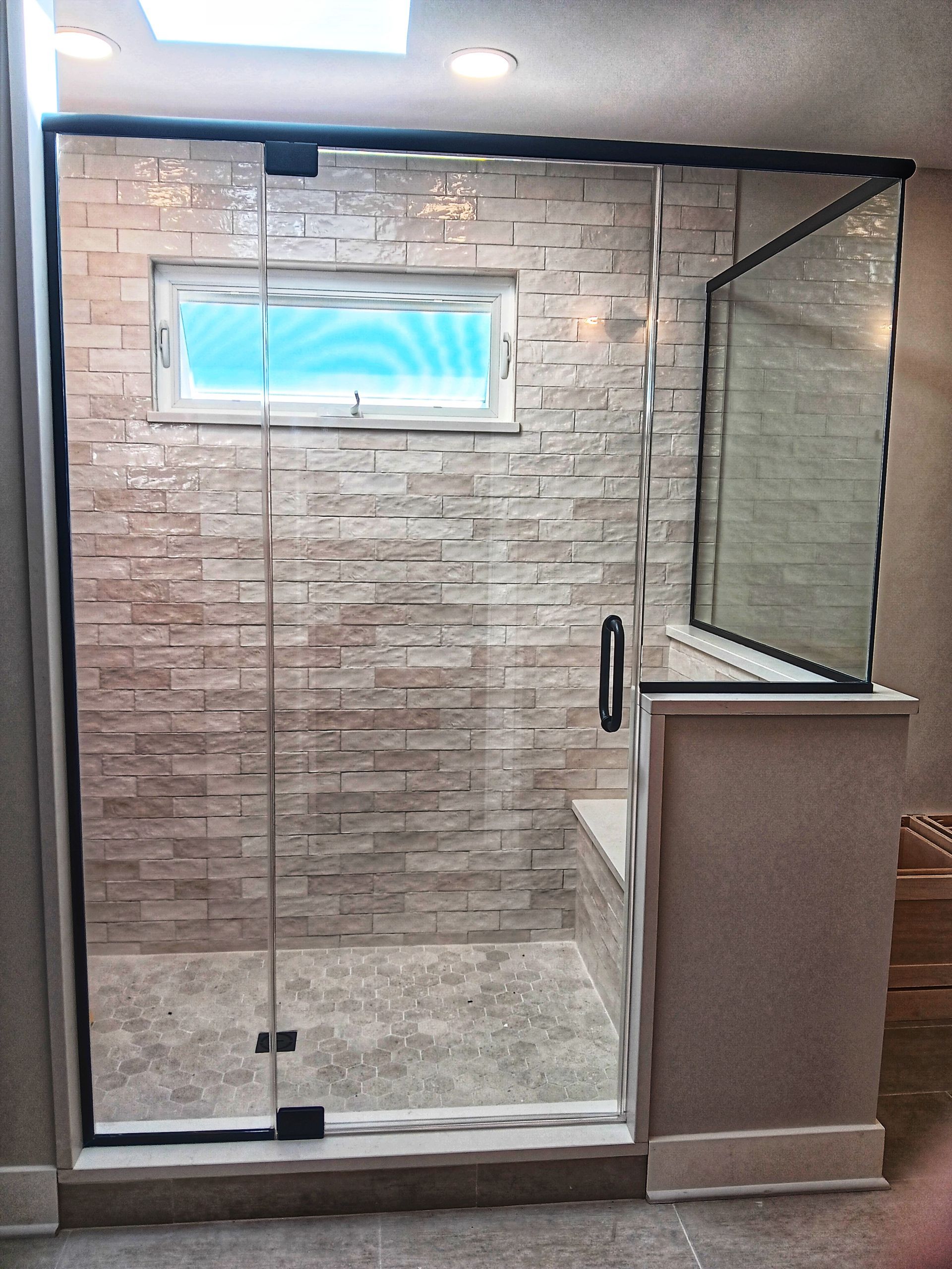 Shower with glass door and stone tile walls, small window, and seat.