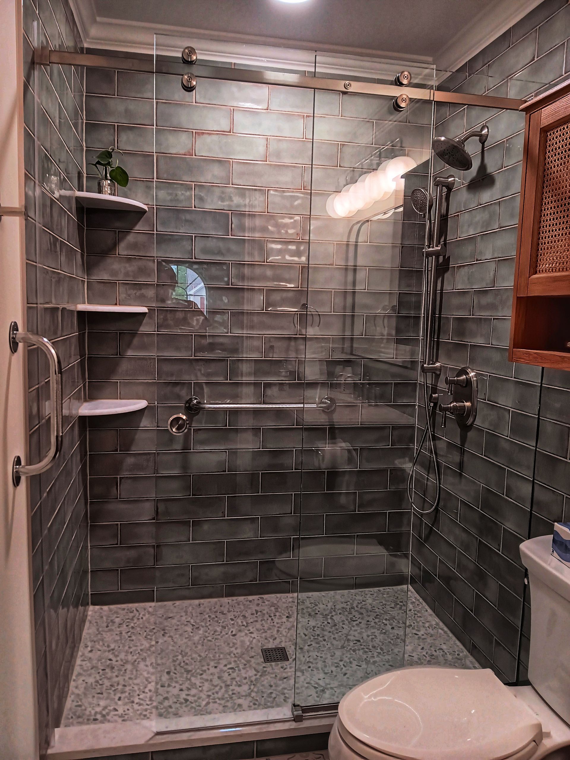 Shower with gray textured tile walls, glass door, and white fixtures.