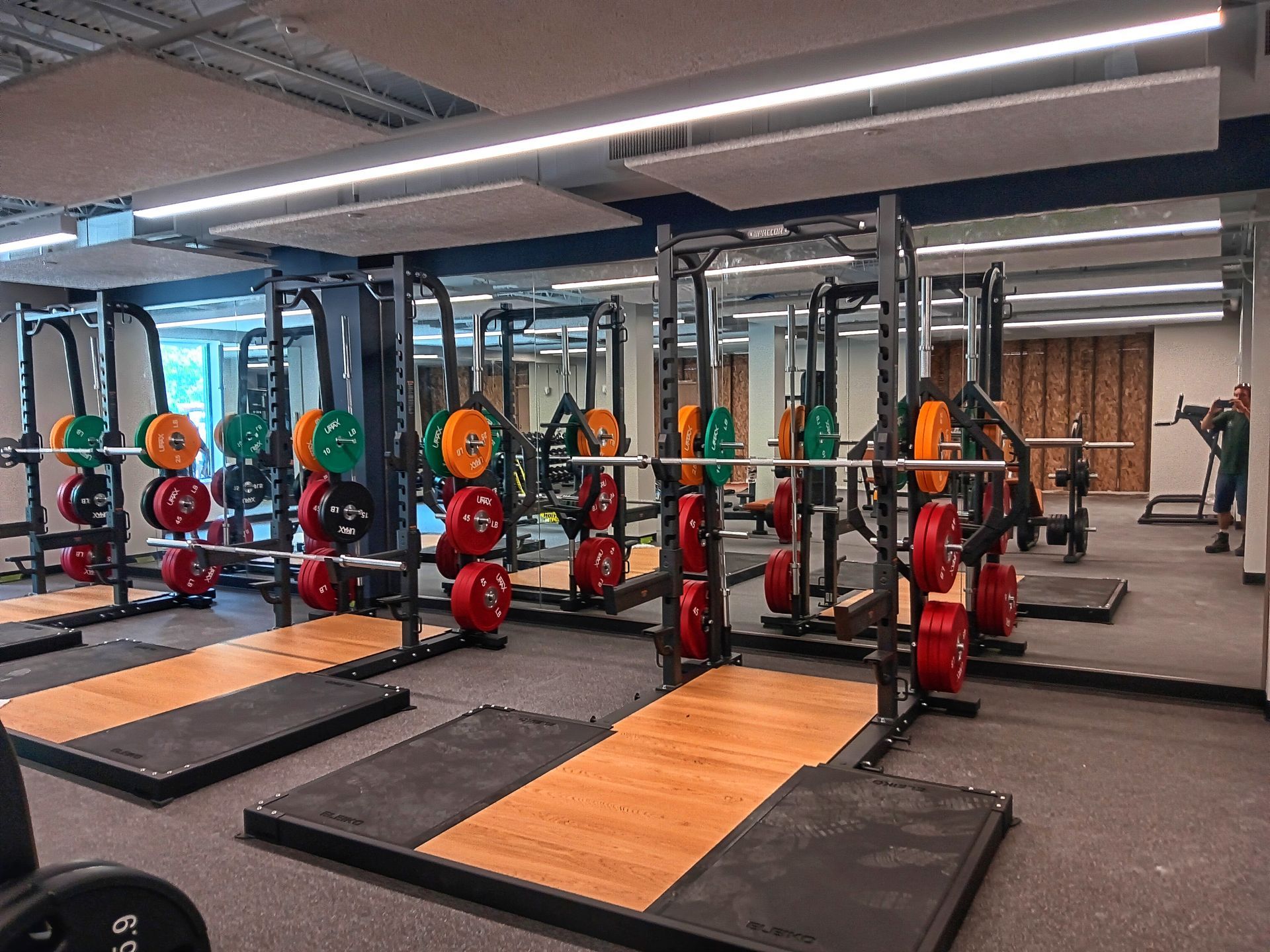 Weightlifting gym with squat racks, weights, and people working out.