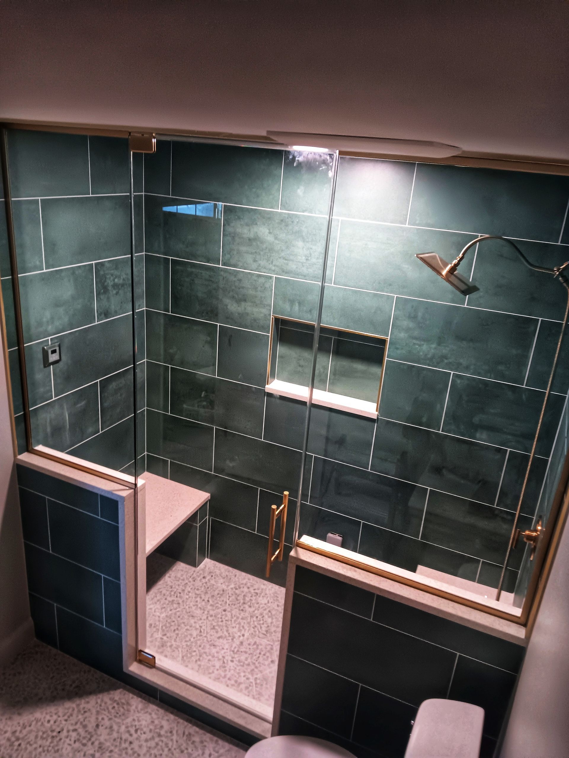 Green tiled shower with glass door, gold fixtures, and a built-in bench.