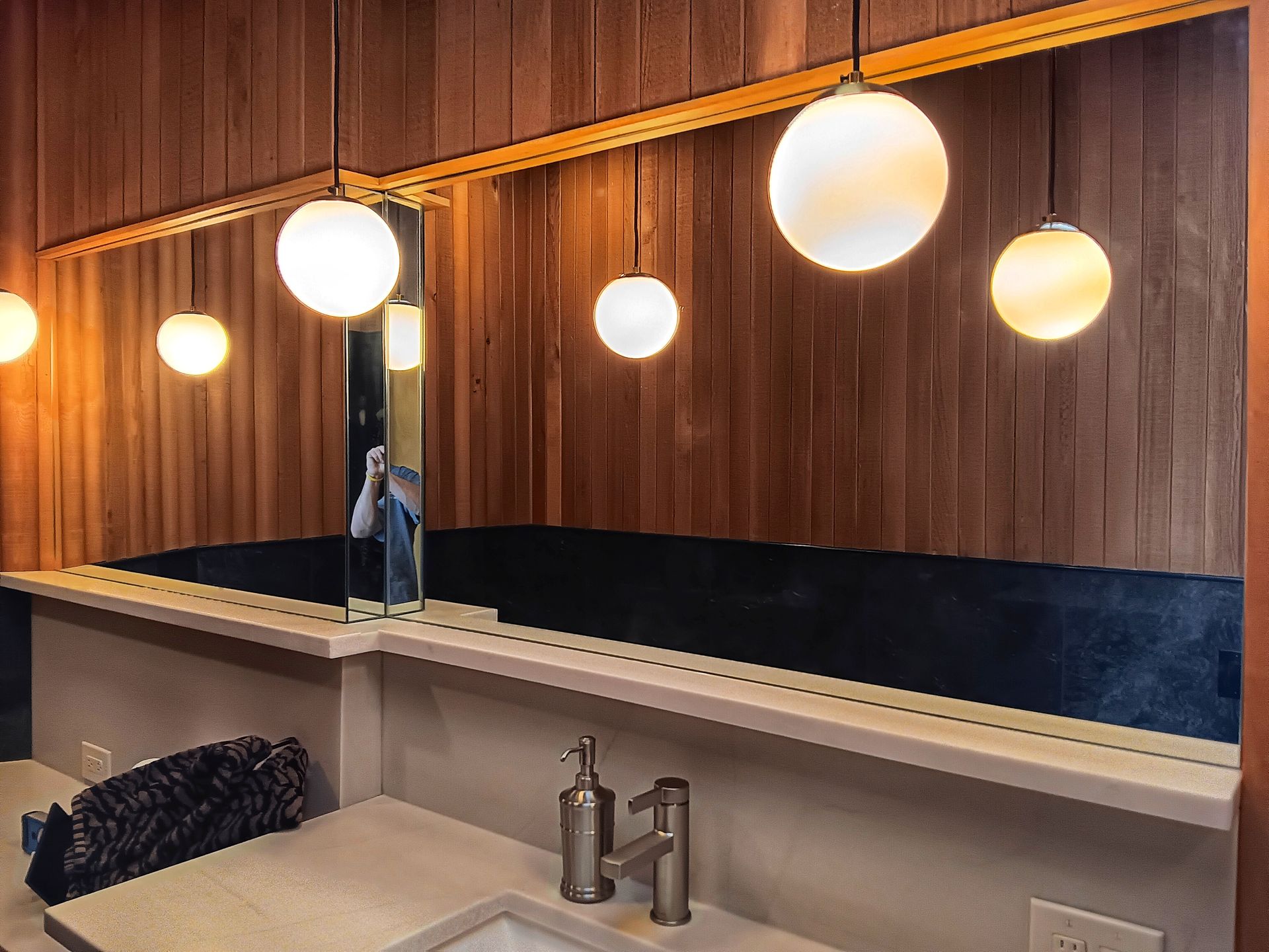 Bathroom with wood paneling, glowing globe lights, a mirror, and sink.