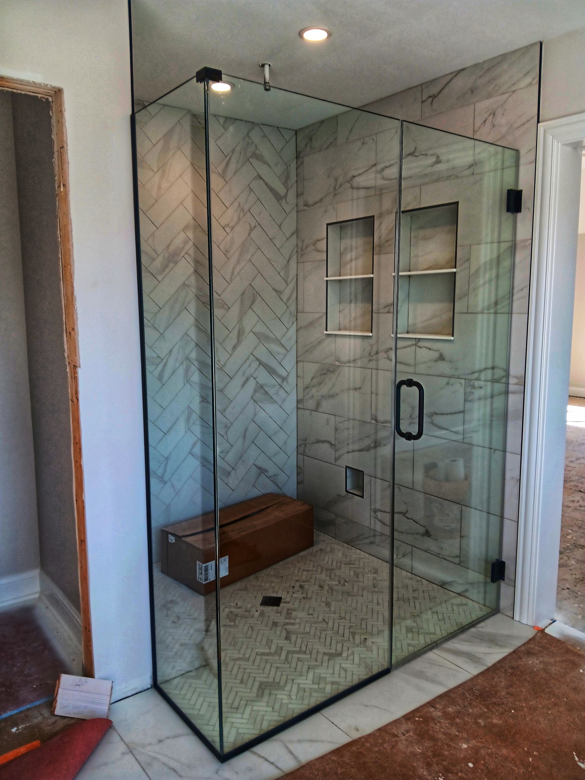 Modern glass-enclosed shower with tiled walls, shower niche, and a wooden bench.