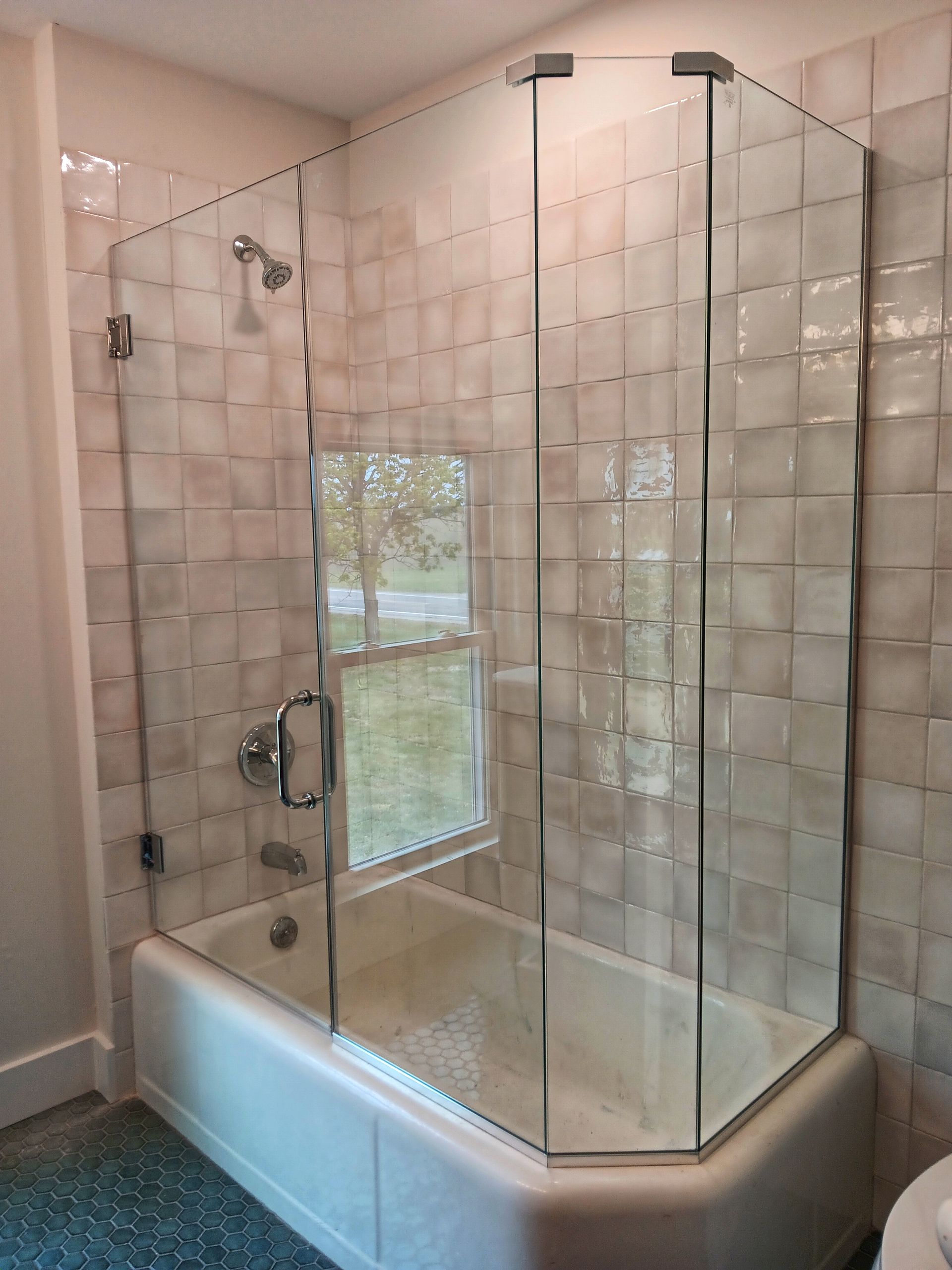 Glass shower enclosure over a white bathtub, featuring a window and textured tile backdrop.