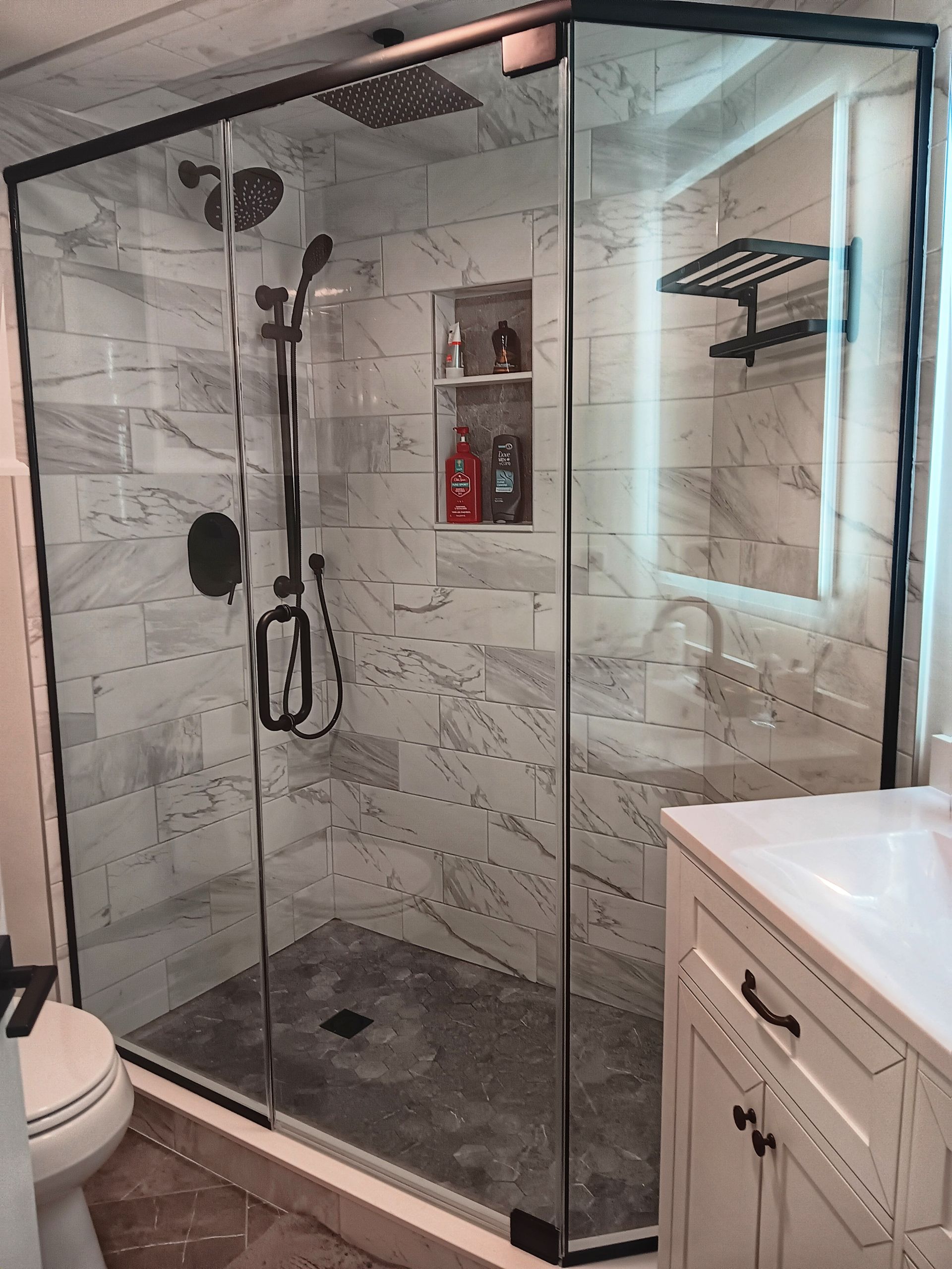 Modern bathroom with glass shower enclosure, marble-like tiled walls, and white vanity.