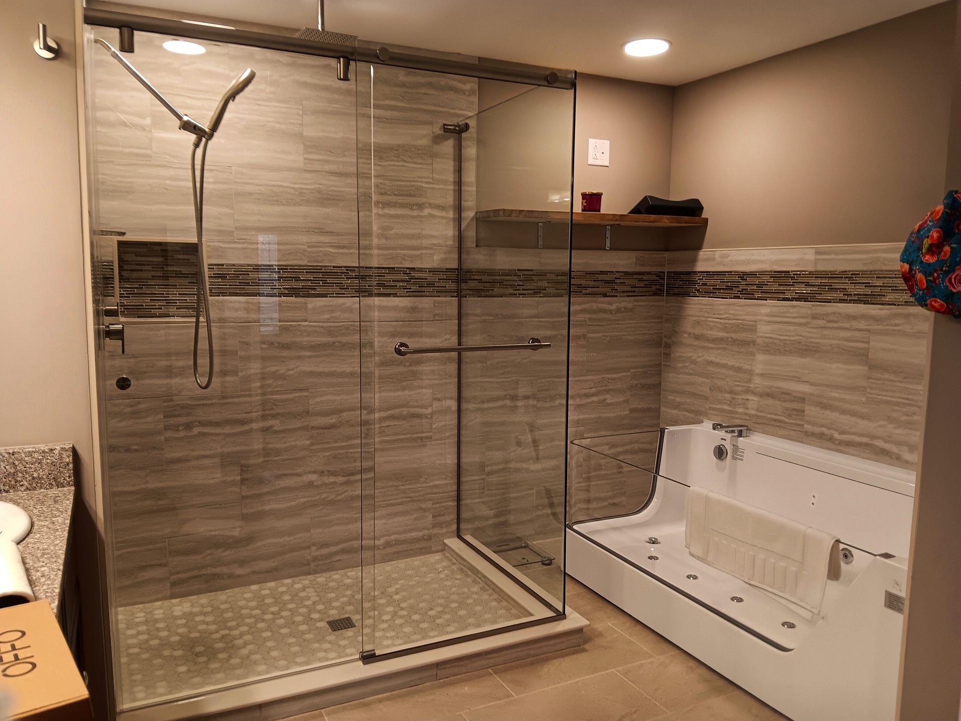 A modern bathroom with a glass shower, tiled walls, and a built-in tub with a towel.