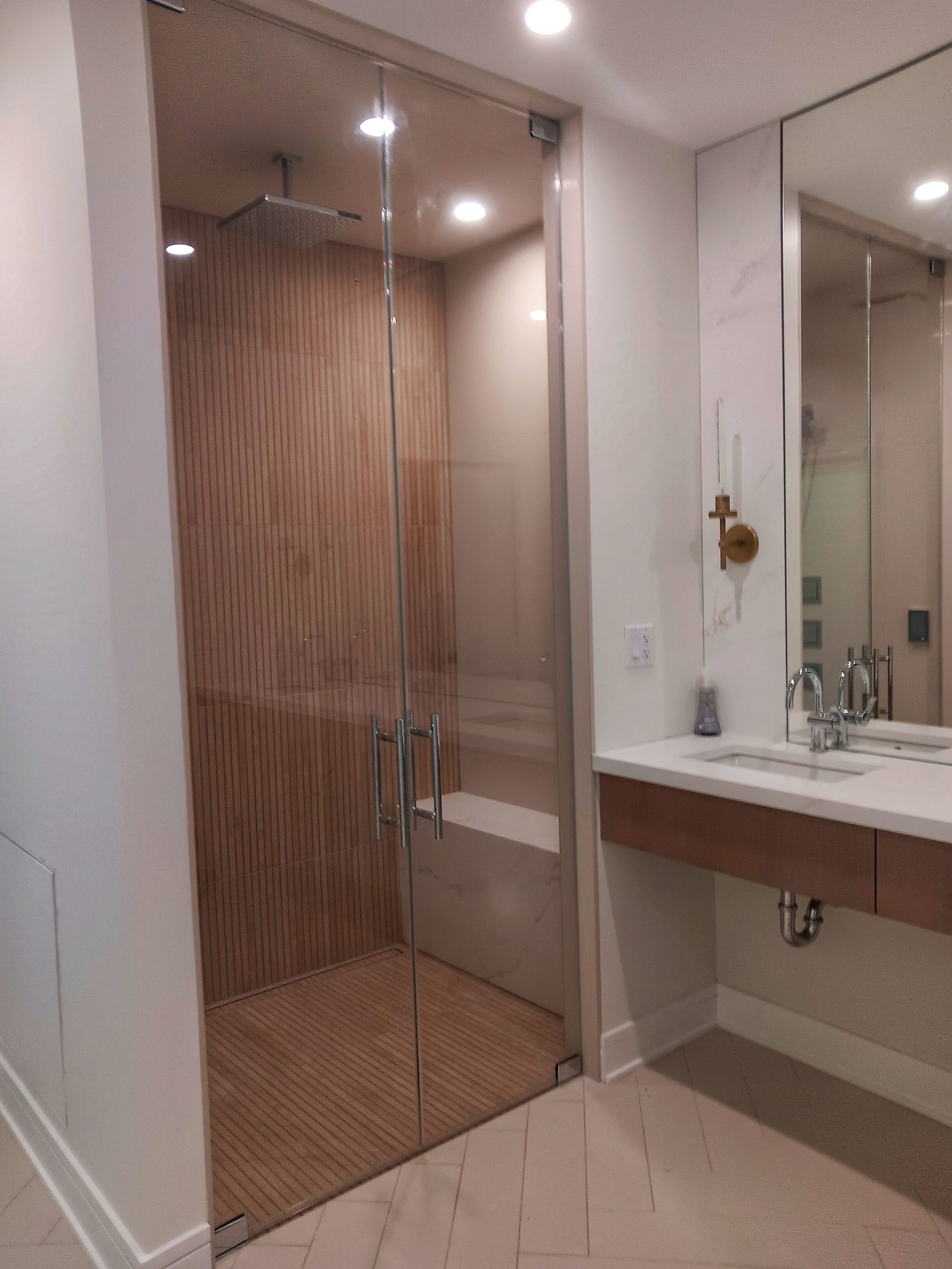 A modern bathroom with a glass shower and wooden accent wall. Vanity and mirror to the right.