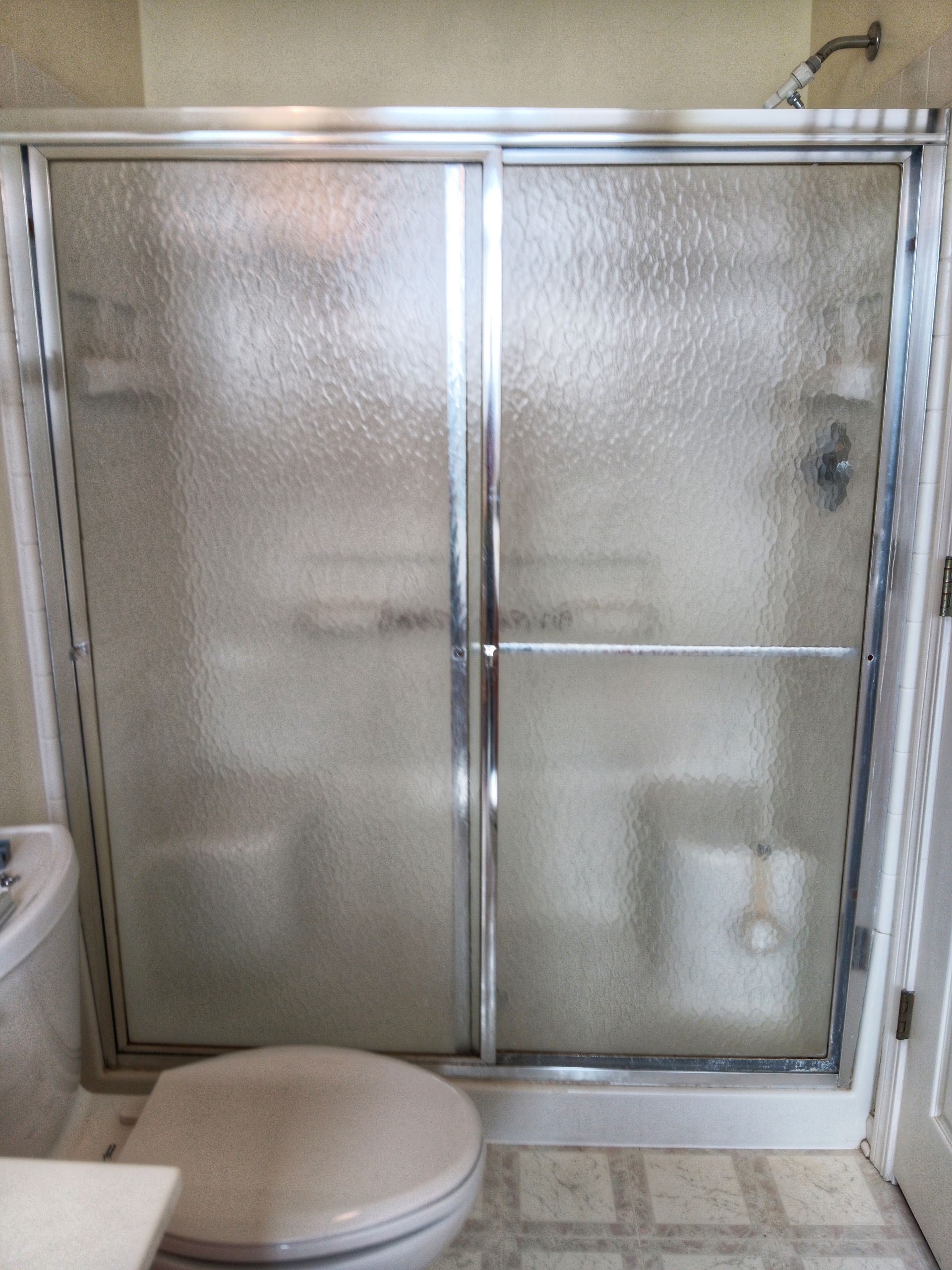 Shower with frosted glass doors, chrome frame, beside a toilet in a bathroom.
