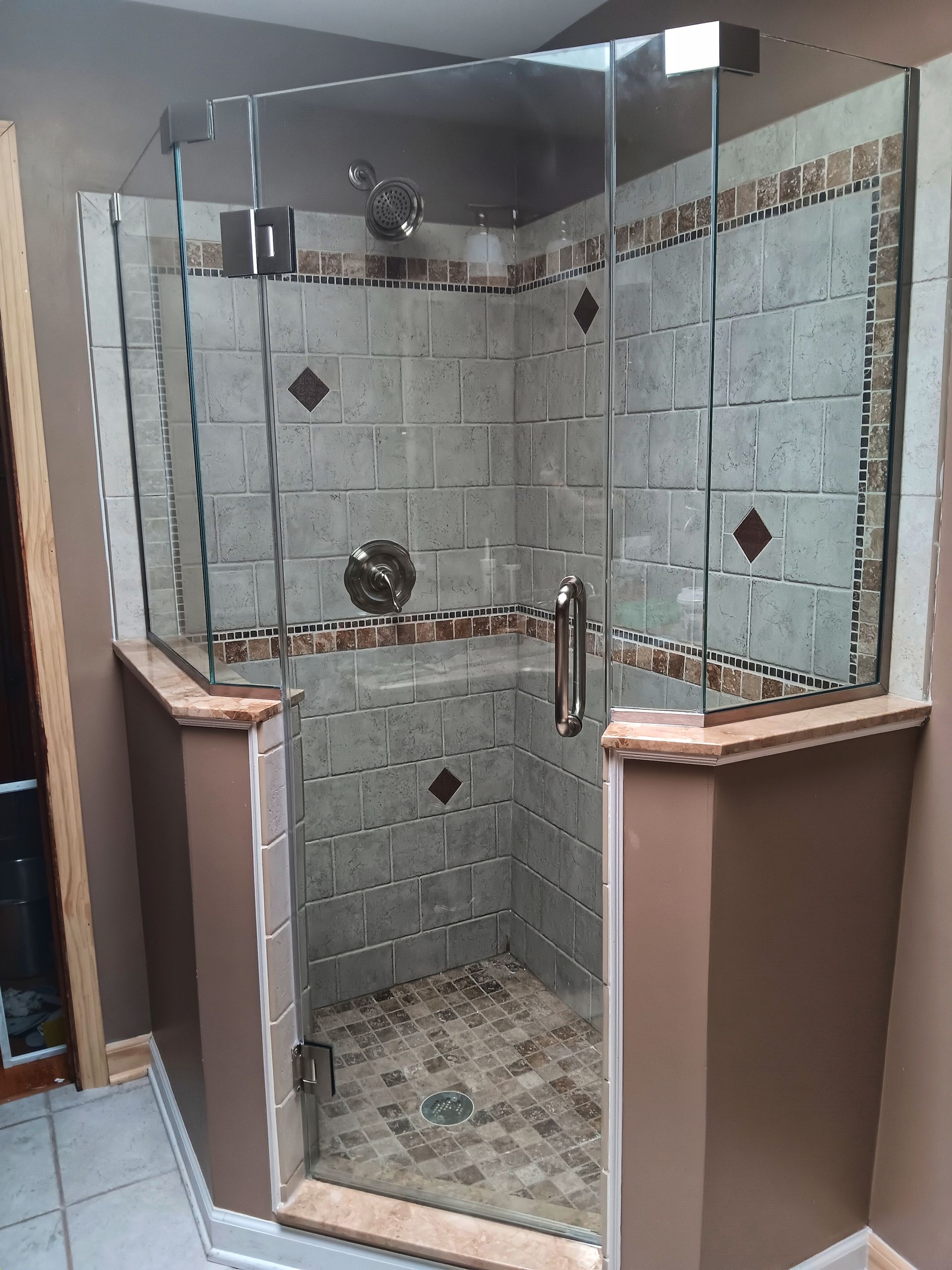 Glass shower enclosure with brown and tan tile, brown walls, and chrome fixtures.
