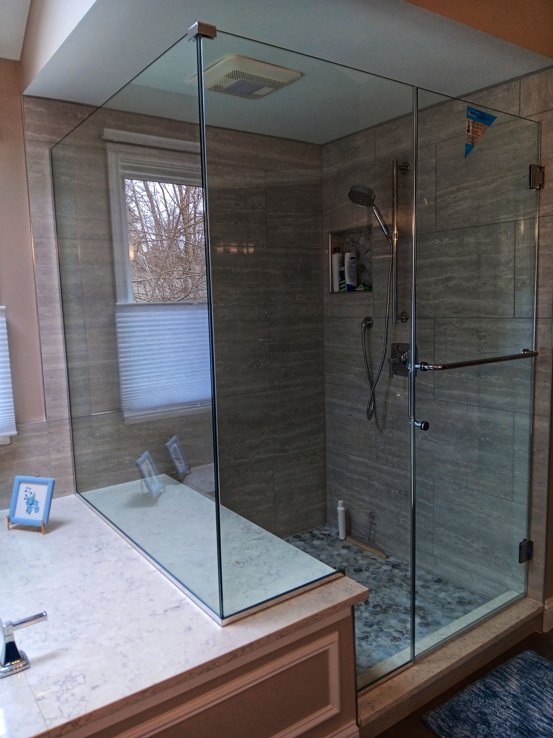 A glass shower enclosure in a bathroom with beige tile walls and a window.