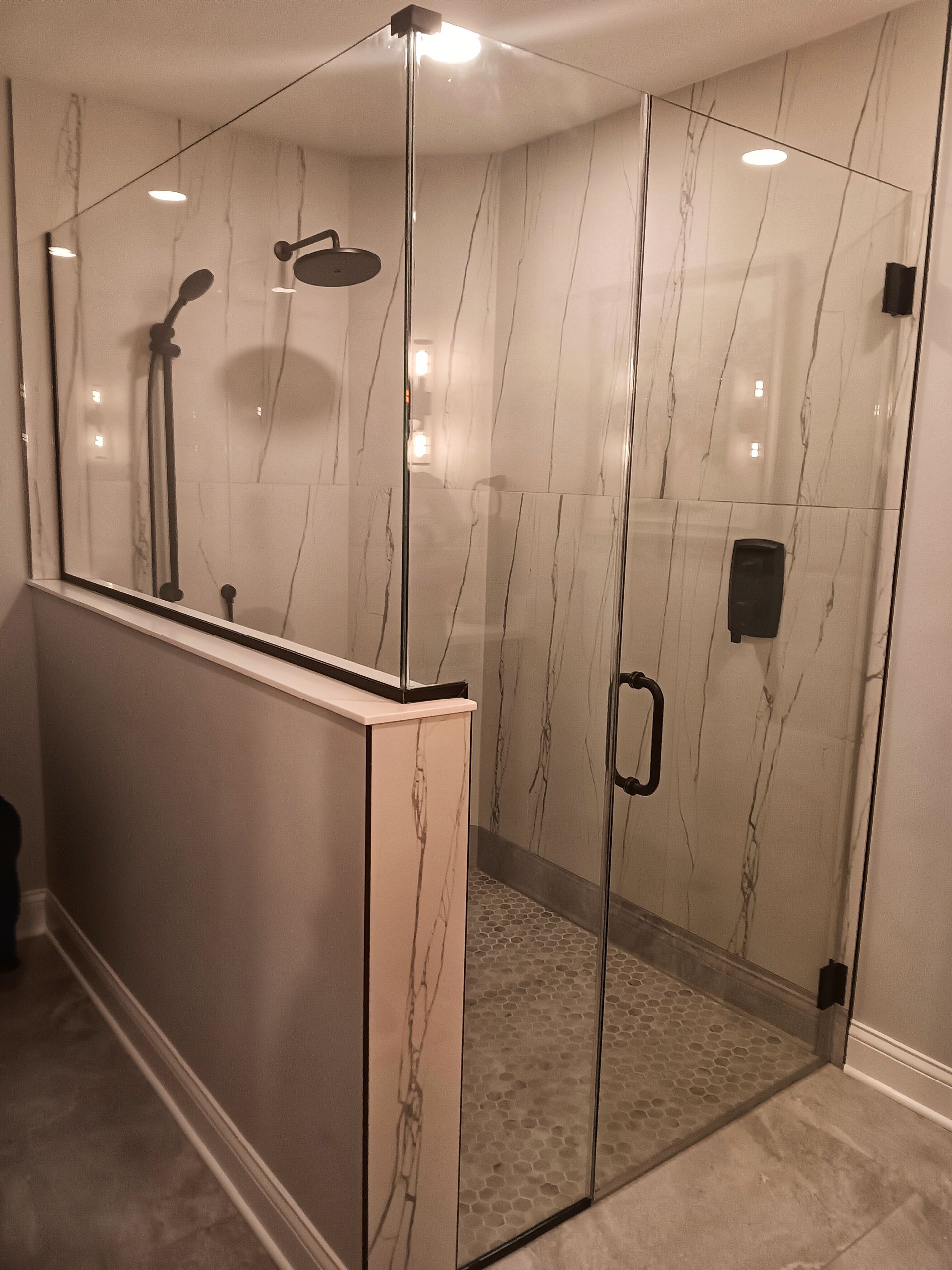 Glass shower enclosure with gray and white tile, shower head, and door.