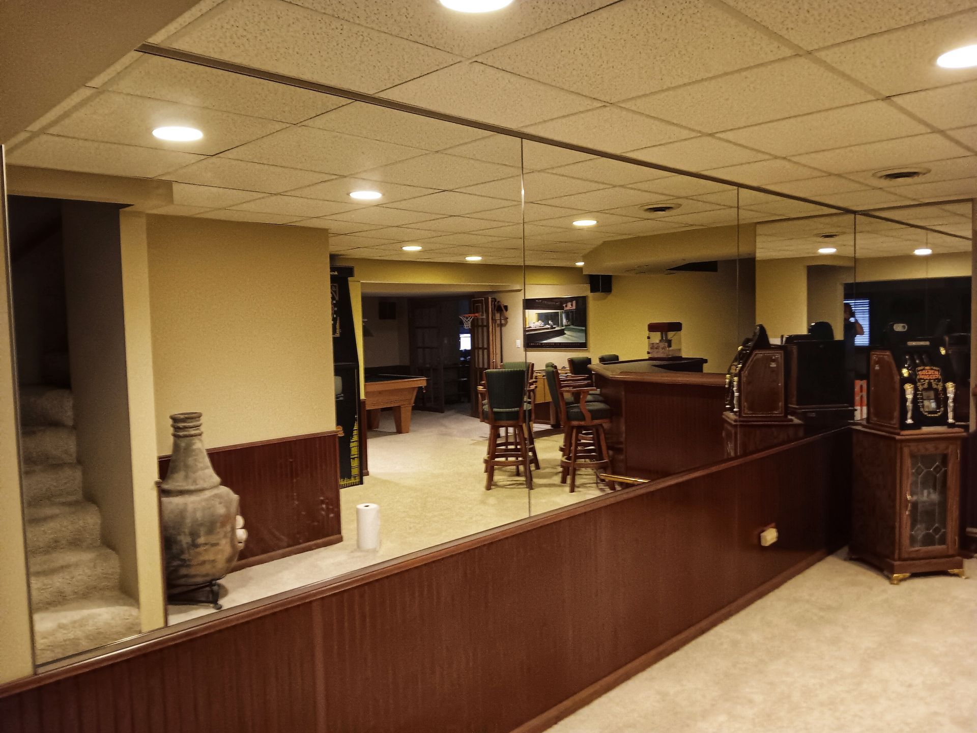 Basement with a bar, mirrored wall, stairs, and a decorative vase.
