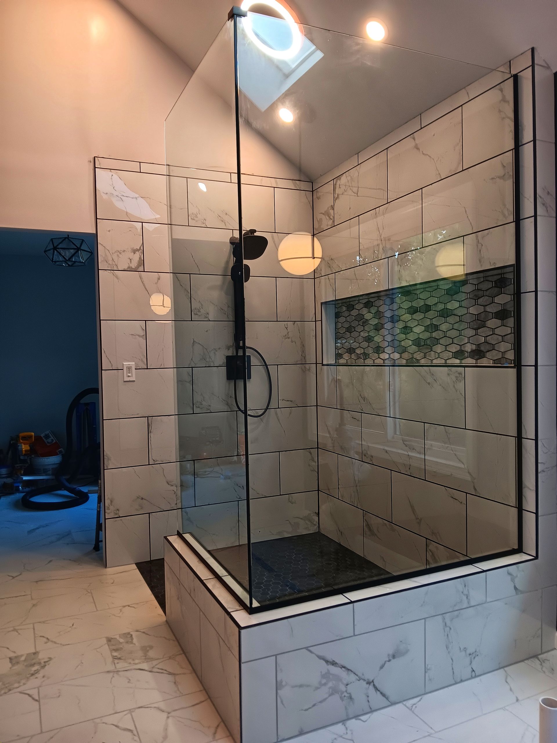 Newly renovated shower with glass door and black fixtures. Tile walls and floor. Skylight overhead.