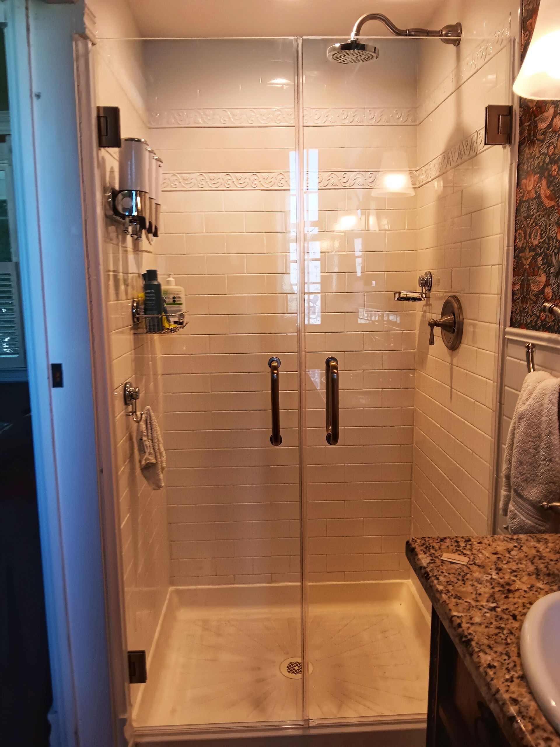 Glass shower with frosted stripes, dark fixtures, and a granite countertop.