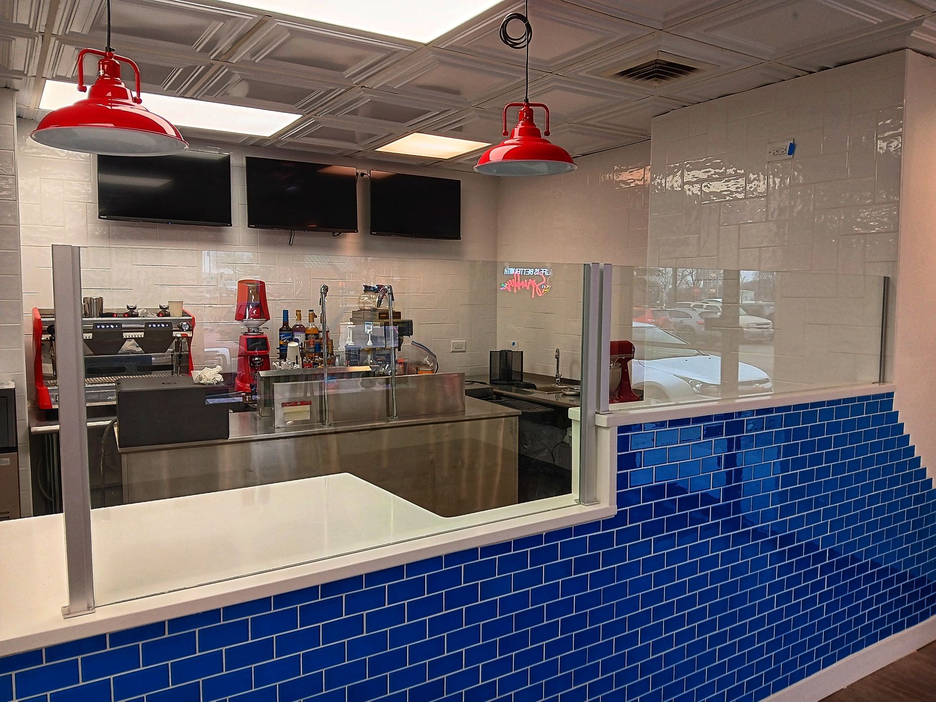 Blue-tiled cafe interior with red pendant lights, stainless steel counter, and clear divider at the counter.