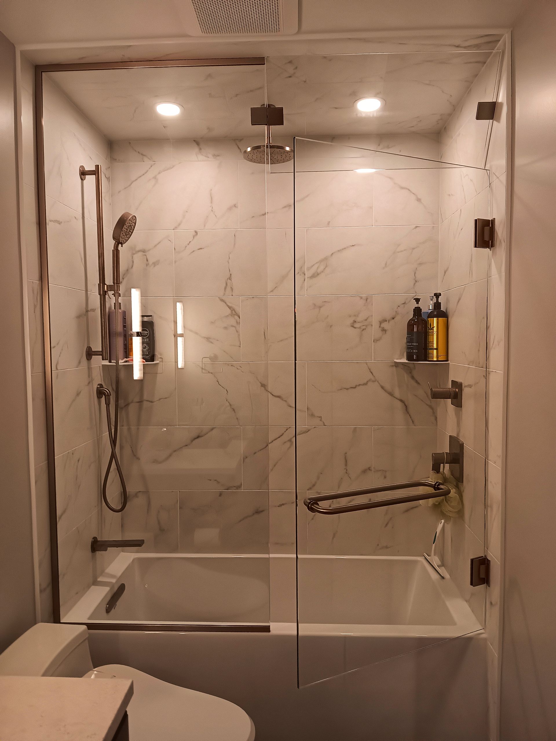 Shower with glass doors and bronze fixtures, built-in to the bathroom, with a bathtub.