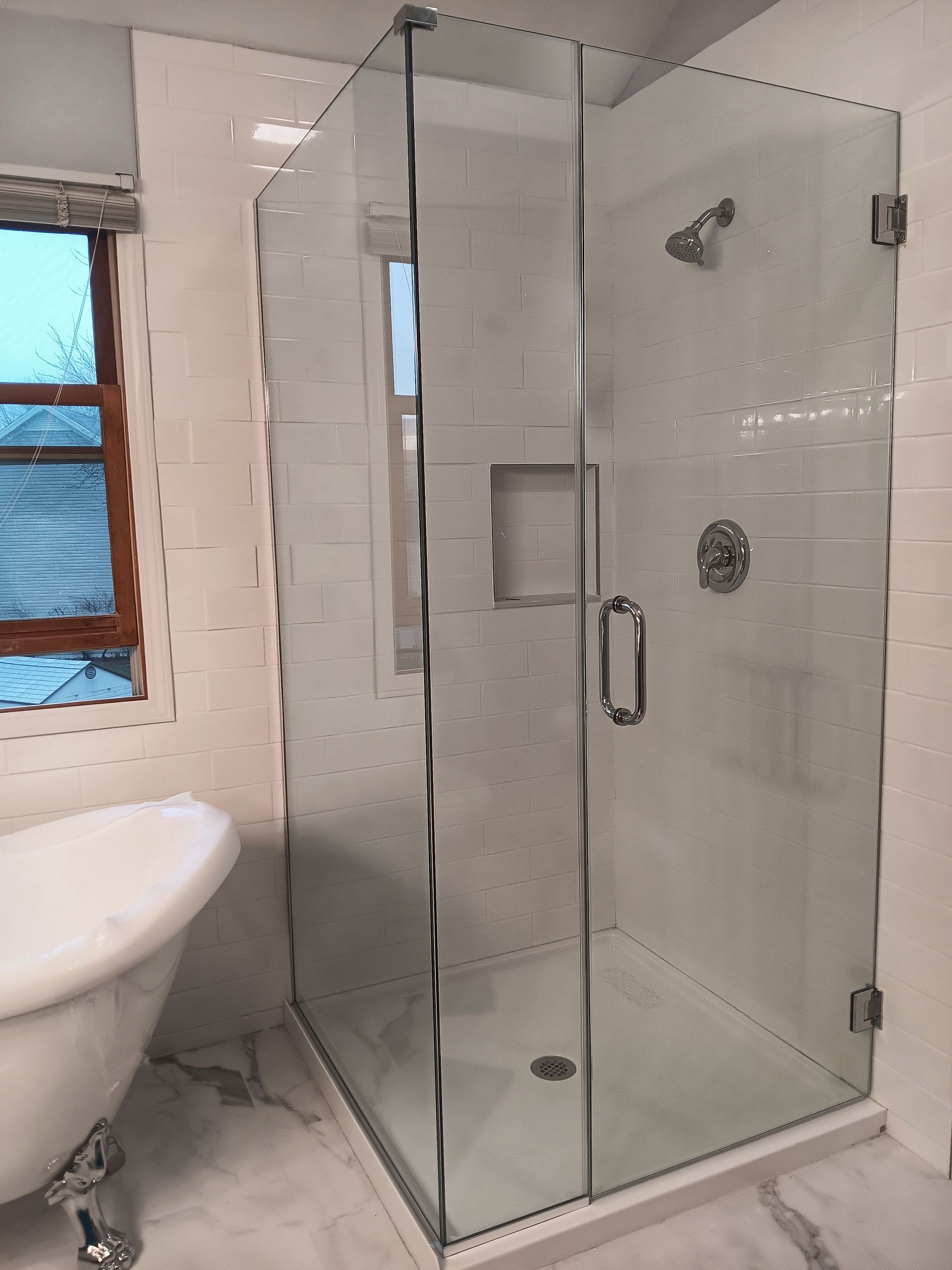 Modern glass shower enclosure in a bright white bathroom with a clawfoot tub.