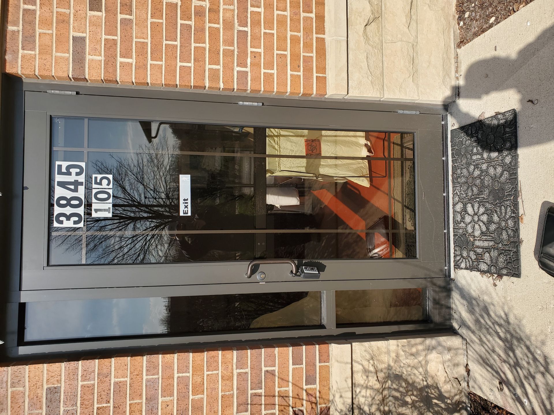 A grey apartment door with the number 3845 105. Brick wall, concrete, and a welcome mat.