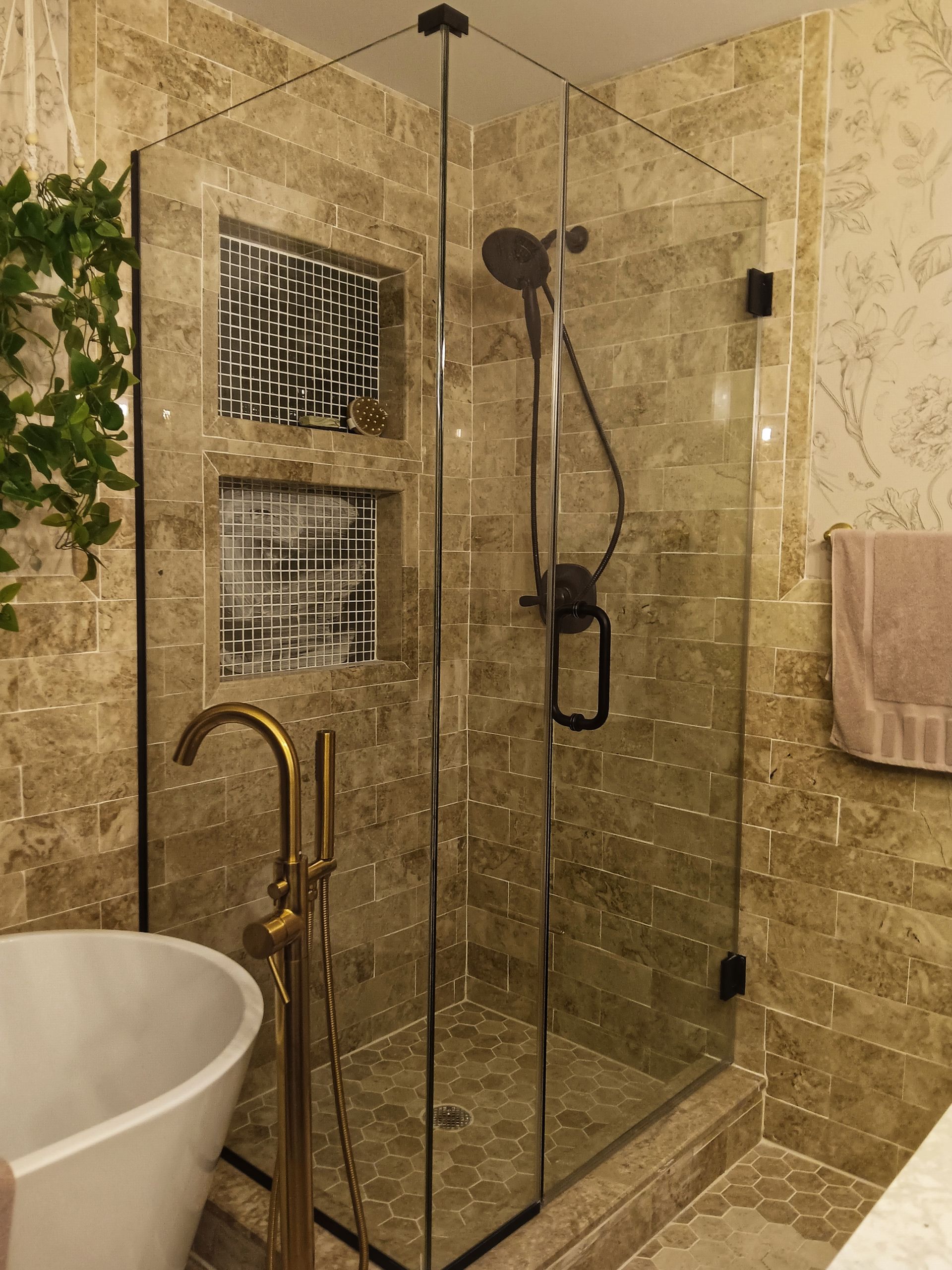 Bathroom with glass shower, gold fixtures, and beige tile.