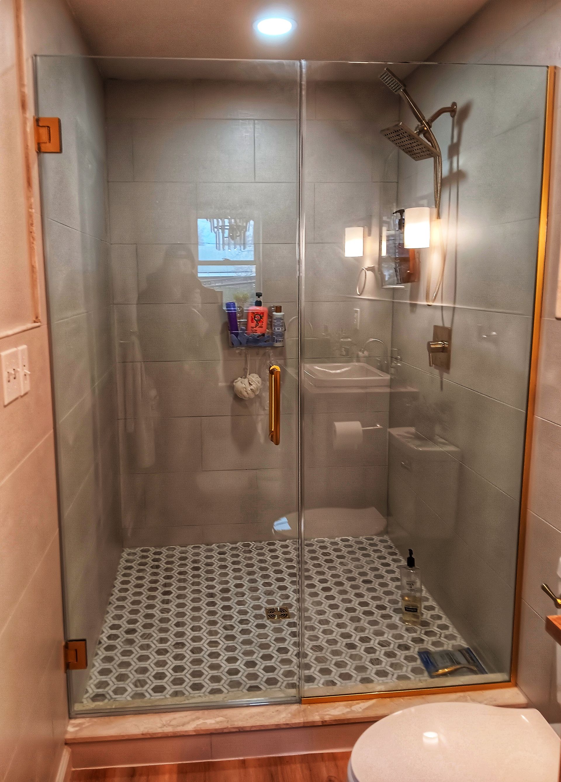 Shower stall with glass door, gray tile, bronze fixtures, stone floor.