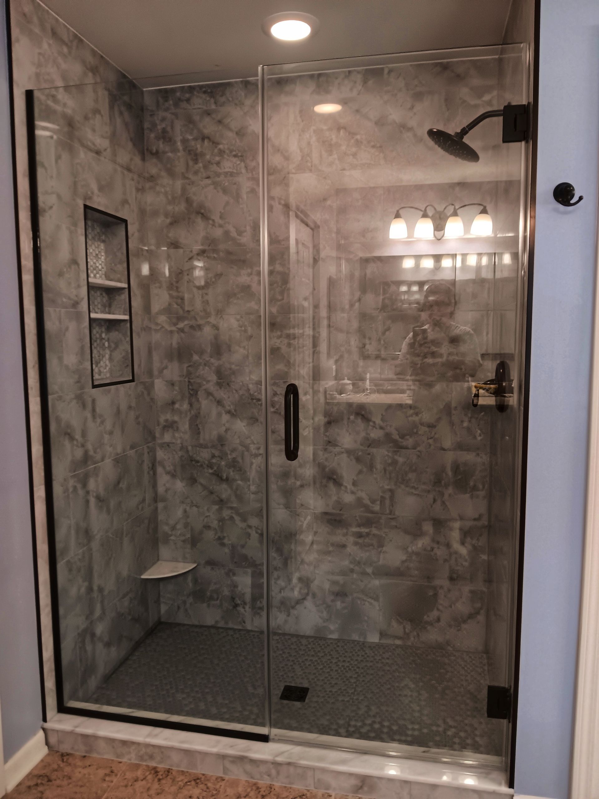 Modern shower with glass door, gray marble-look walls, black fixtures, recessed shelf.