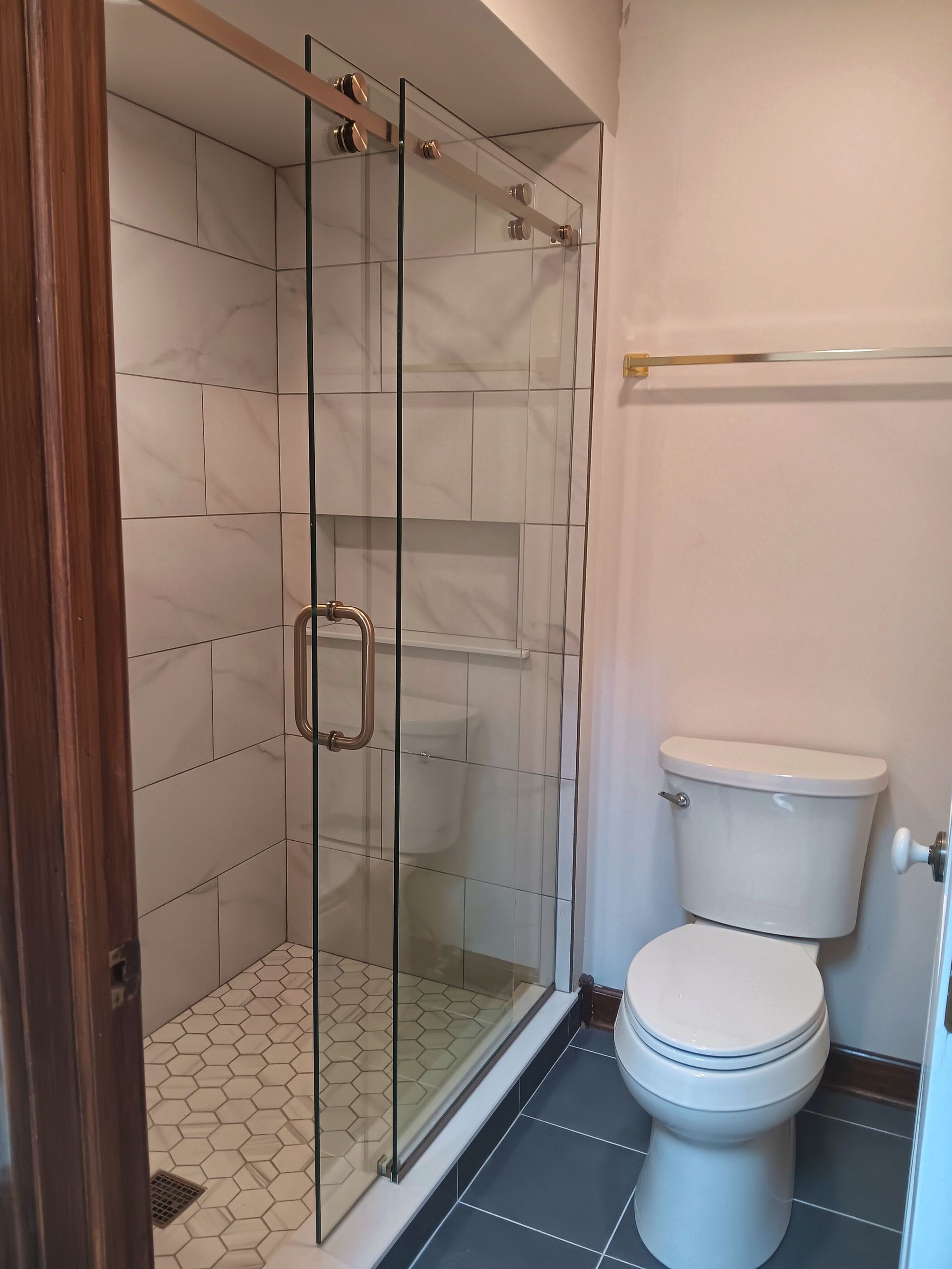 Bathroom with glass shower, white toilet, and tile floors.
