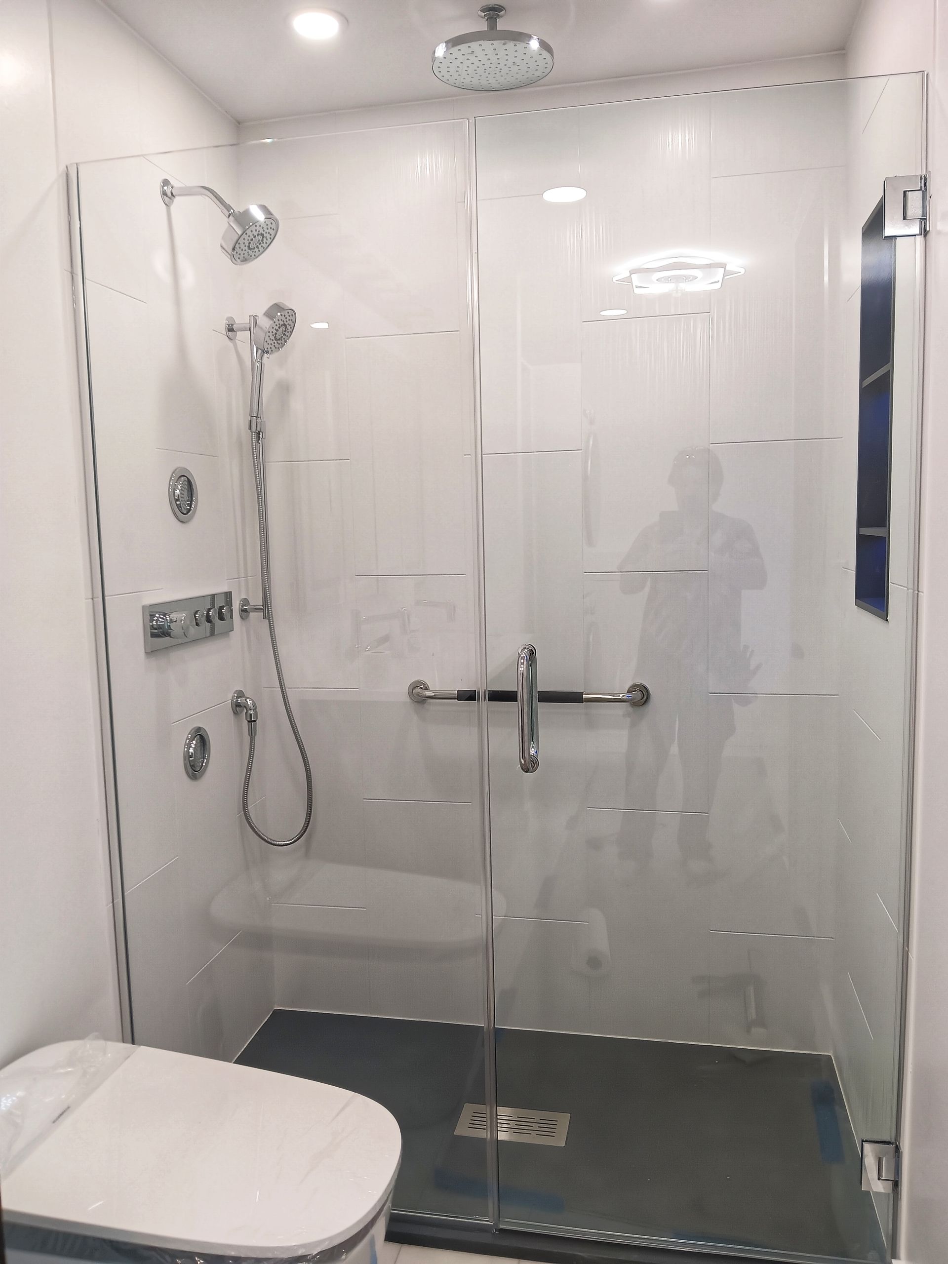 Modern bathroom with glass shower doors, white tile, and a toilet.