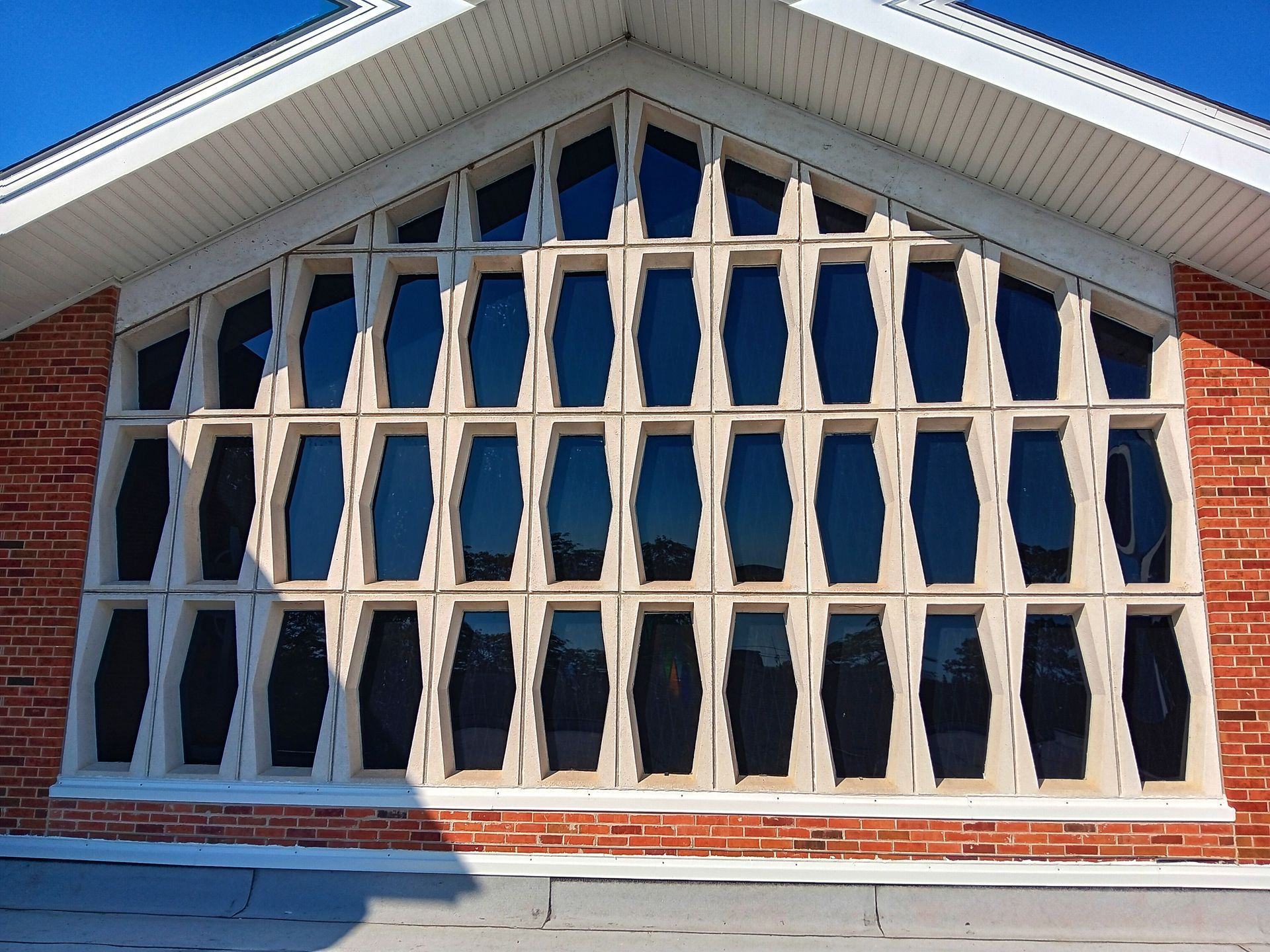 Large, arched window with dark panes, set in a red brick building, blue sky backdrop.