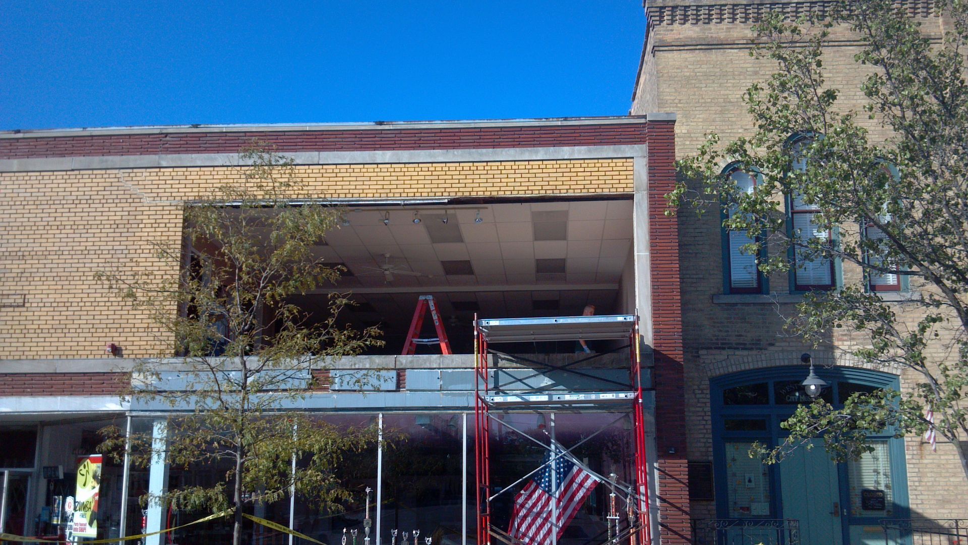 Building facade undergoing renovation, with visible scaffolding, American flag, and yellow caution tape.
